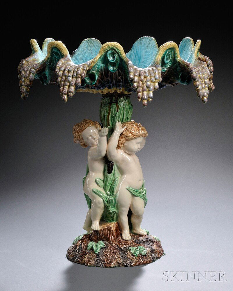 Hugo Lonitz Majolica Figural Compote, Germany, thi: Hugo Lonitz Majolica Figural Compote, Germany, third quarter 19th century, polychrome enamel decorated and modeled as a naturalistic bowl set atop a stem surrounded by three cherubs, impressed factory