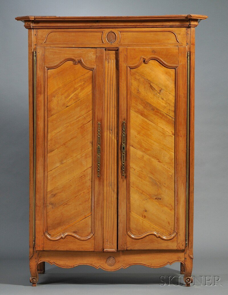 French Provincial Armoire, 19th century, of typica: French Provincial Armoire, 19th century, of typical form with a shaped projecting cornice, a central ovoid medallion to upper frieze and apron, canted and fluted corners, and two doors: each with bras