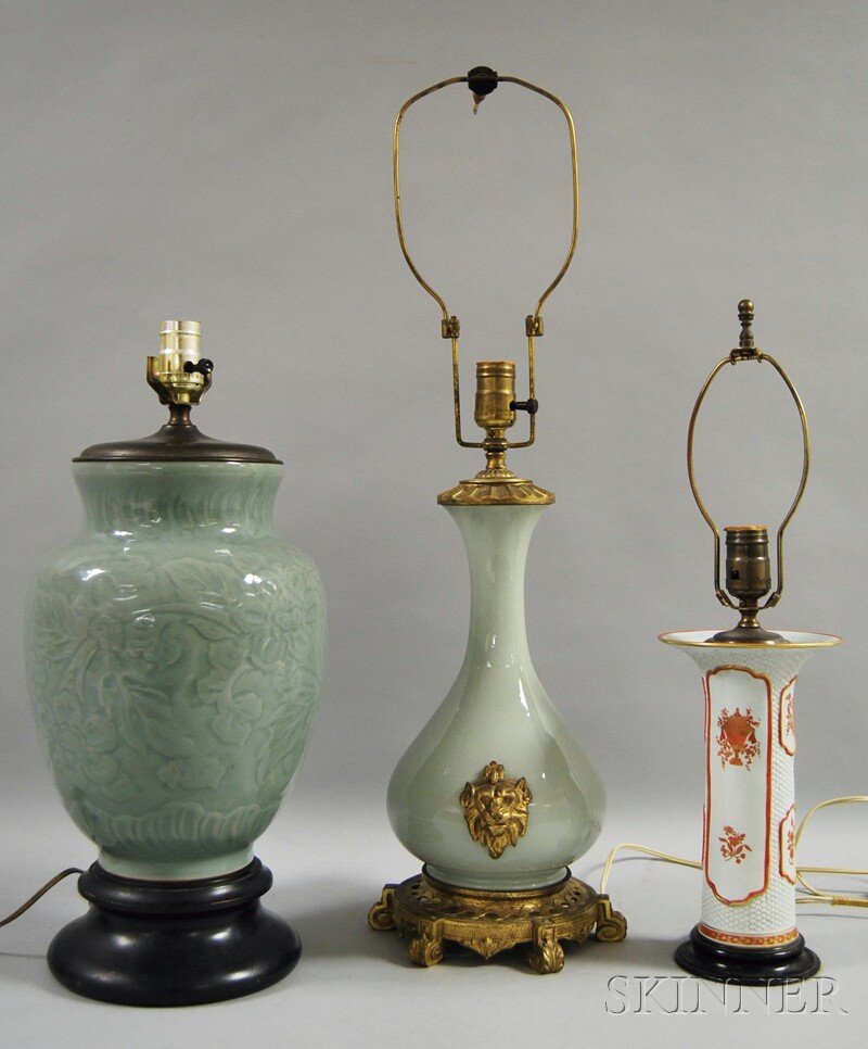 Three Asian Ceramics Mounted as Table Lamps, a cel: Three Asian Ceramics Mounted as Table Lamps, a celadon porcelain ginger jar-form with leaves and flowers in low relief on a wooden base, a celadon porcelain baluster-form lamp with brass lion mask mou