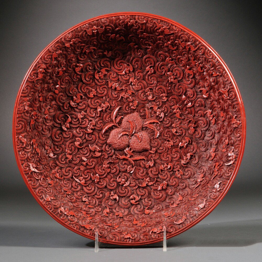Plastic Faux Cinnabar Plate, China, the interior molded: Plastic Faux Cinnabar Plate, China, the interior molded with peaches surrounded by bats against a swirl-patterned ground, the exterior with flowers against a geometric ground, base with "Qing Qianlong
