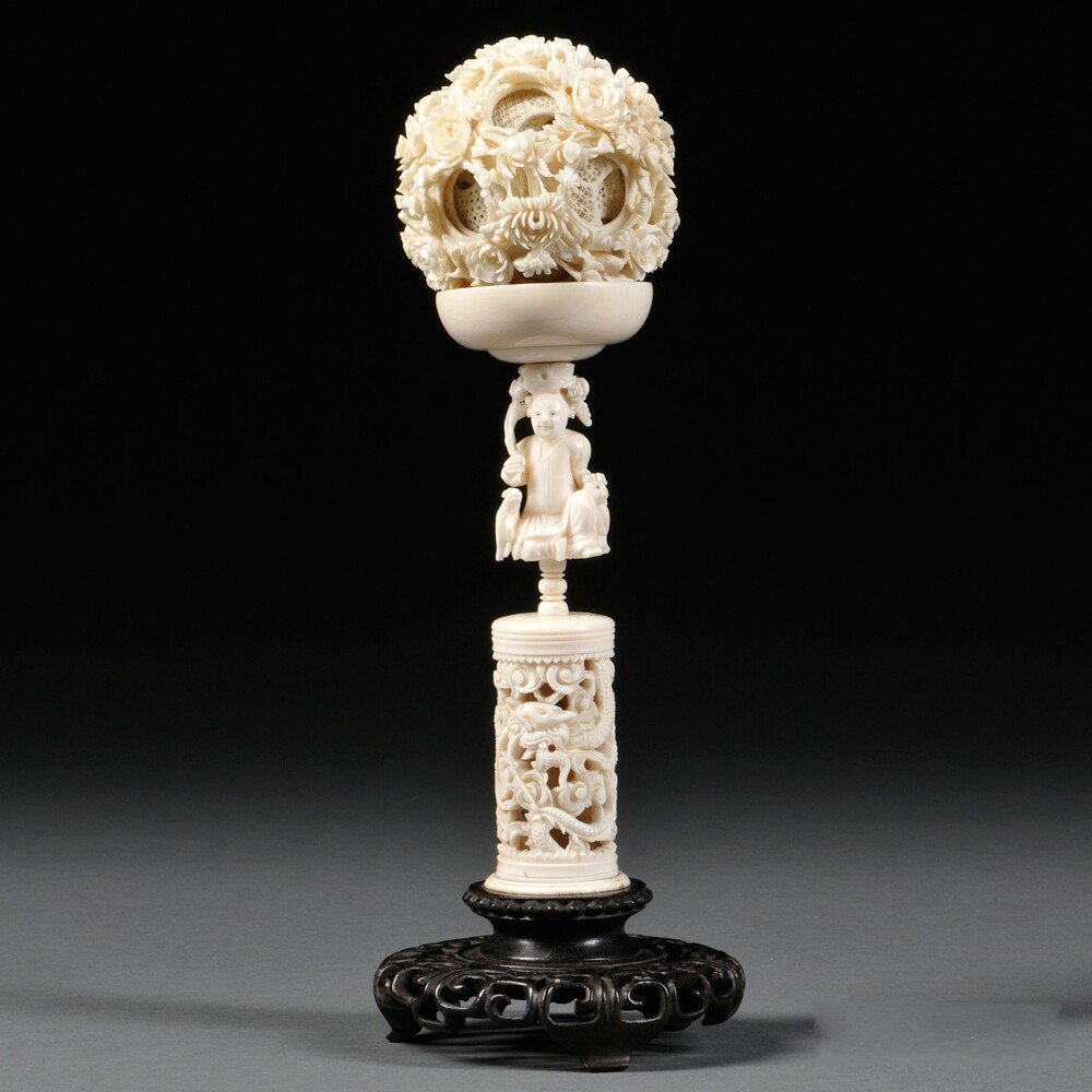 Ivory Puzzle Ball and Stand, China, 20th century, the: Ivory Puzzle Ball and Stand, China, 20th century, the ball with floral design in deep relief, dia. 3; the stand with an openwork dragon column, surmounted with a seated figure with a dish-shaped holde