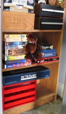 Small shelf with contents:: Small shelf with contents: Magvox VHS & DVD player with VHS tapes & CDs, cassette tapes, games doubloons, stuffed animals, 20th century