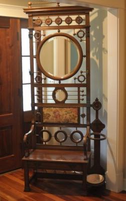 Antique walnut hall tree, ornate top rail, 2 oval: Antique walnut hall tree, ornate top rail, 2 oval beveled mirrors, upholstered back with nail head design, curved arms, 4 brass hooks, umbrella stand with cast iron dish, 1 drawer under the seat, bass