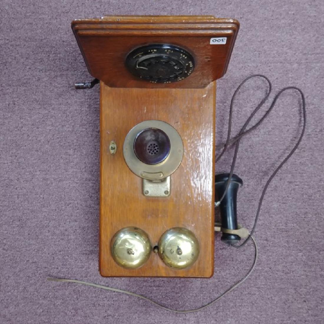 Antique Oak Wall Telephone: Brass bells, black rotary dial, wind up on the side. Very old breakage at the bottom back right of the case as shown in photo. 20-1/2" high