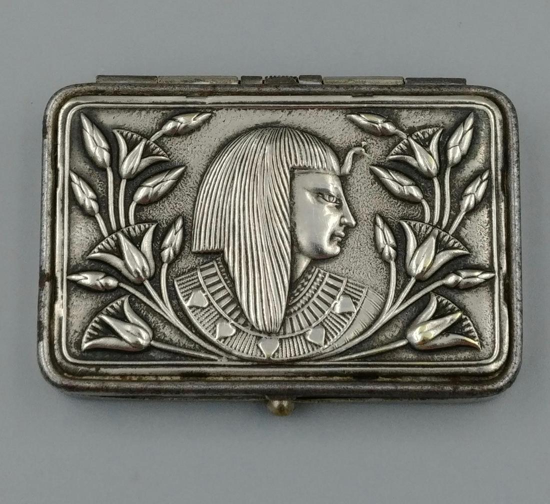 Nickel Plated Egyptian Motif Match Safe: Nickel silver over brass match safe. Top of safe is decorated with the profile of an Egyptian face surrounded by flowers. Push button to open safe. Interior window inside the lid with paper showing ow