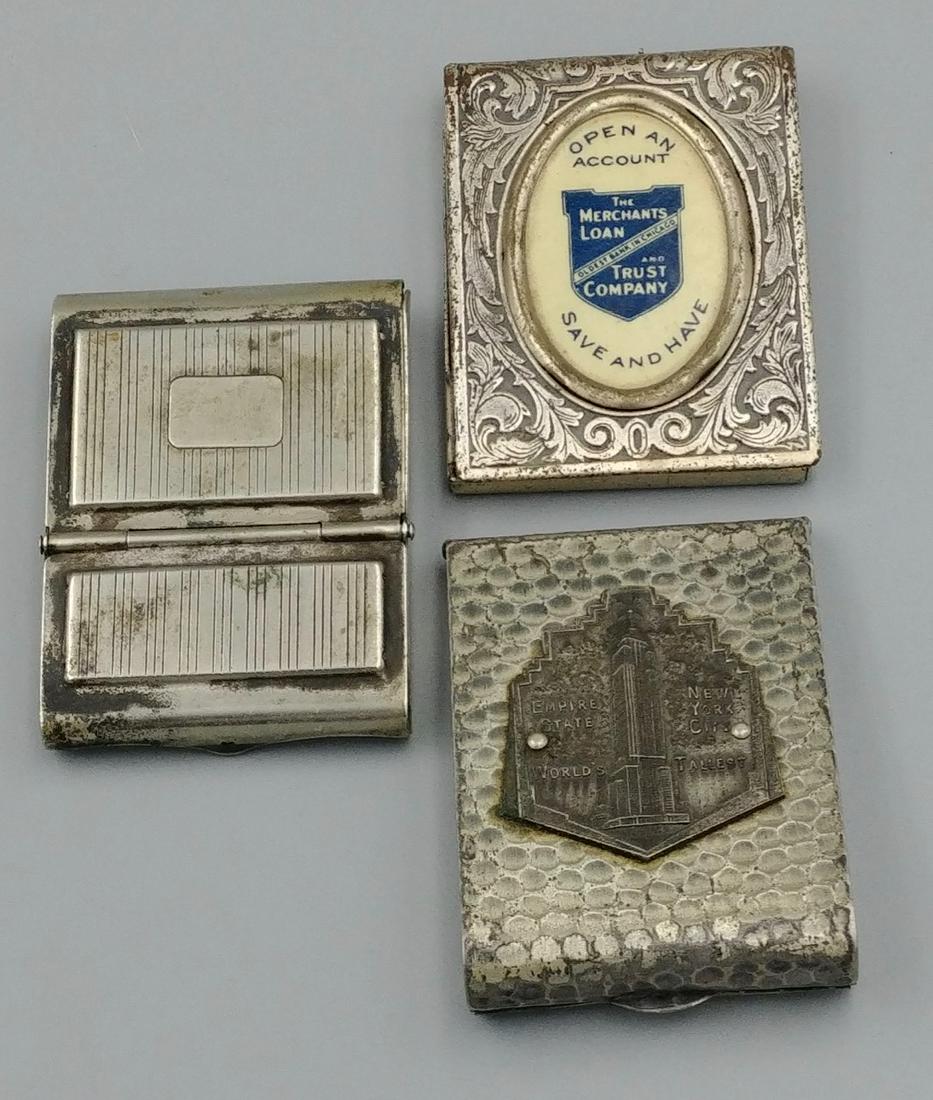 Silvered Matchbook Holders (3): Double compartmented box marked Colgate & Co., New York, USA; Hammered silver Souvenir Empire State Building matchbook; Repousse case with oval advertisement for The Merchants Loan and Trust Company, 