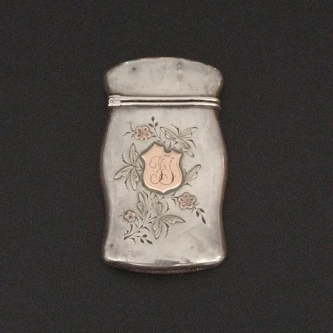 Sterling Silver and Gold Match Safe: Sterling silver (marked on the lip) with gold overlay flowers and shield on the front. Monogrammed FT. Flip top with striker at the base. Allover denting on this piece.