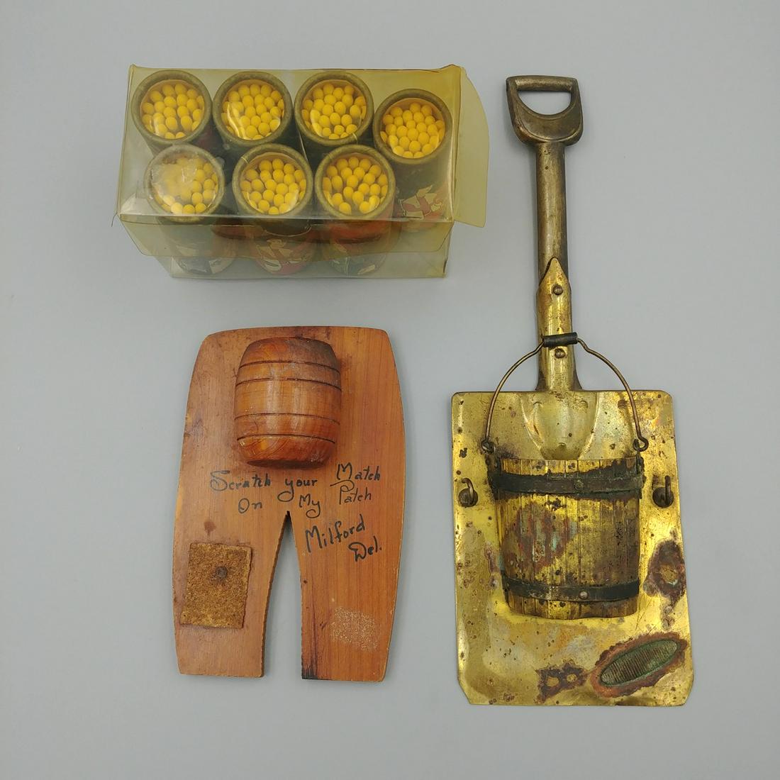 Two Match Holders with Japanese Matches (3): Brass plated wall hanging match holder in the form of a shovel and bucket. Striker to the bottom right of the bucket. Two hooks at the sides. Unmarked.; A wood souvenir holder in the shape of pants wi