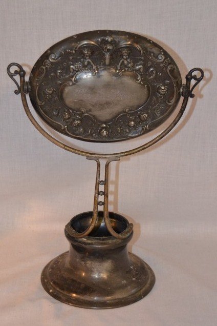 Plated Silver Shaving Mirror: Rosebud and cherub embossed and inscribled Leo A. Swan. Monogrammed at the base. Circular stamp at base for Wilcox Silverplate, Made in USA. Small damage to top of the mirror as seen in photo. 14-1/2"