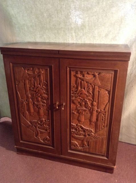 Oriental Carved Wooden Rolling Bar Cabinet: Oriental carved wood self contained bar cabinet on casters. Opens to reveal a storage compartment and drawers for wines, liquors, glasses, bar tools and the like. Green marble flip top. Carved figures
