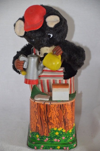 Battery Operated Bear with Coffee Pot Tin Toy: Bear with red cap and striped overalls pouring coffee. Loaf of bread sits on a log. Marked Made in Japan. 9-1/2" high