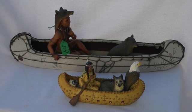 Two Native American Canoe Collectibles: Resin canoe and figure; together with a wood and simulated birch bark canoe with resin Native American and wolf. Missing paddle. 9-1/2"long; 21" long