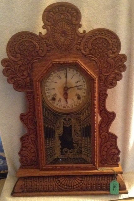 Ingraham Gingerbread Mantle Clock: Ingraham Company, Bristol, Conn. 31 Day clock. Reverse painted on glass depicting two side walls with drapery at the center. Key wound. Heavily carved Oak. Partial paper label at back. 23" high