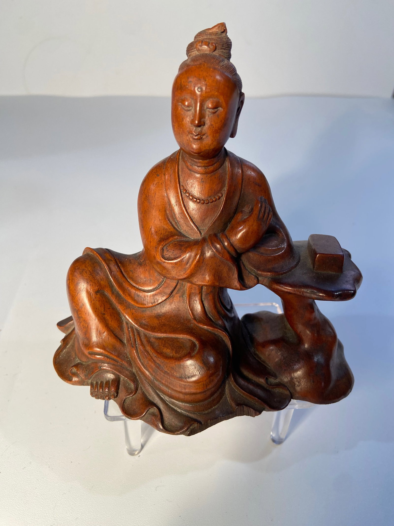 A Chinese boxwood carved seated Guanyin statue: 19th century; The boxwood statue has rich antique patina. The figure is seated in a relaxed pose with one arm resting on a table or stand. Height: 5 inches