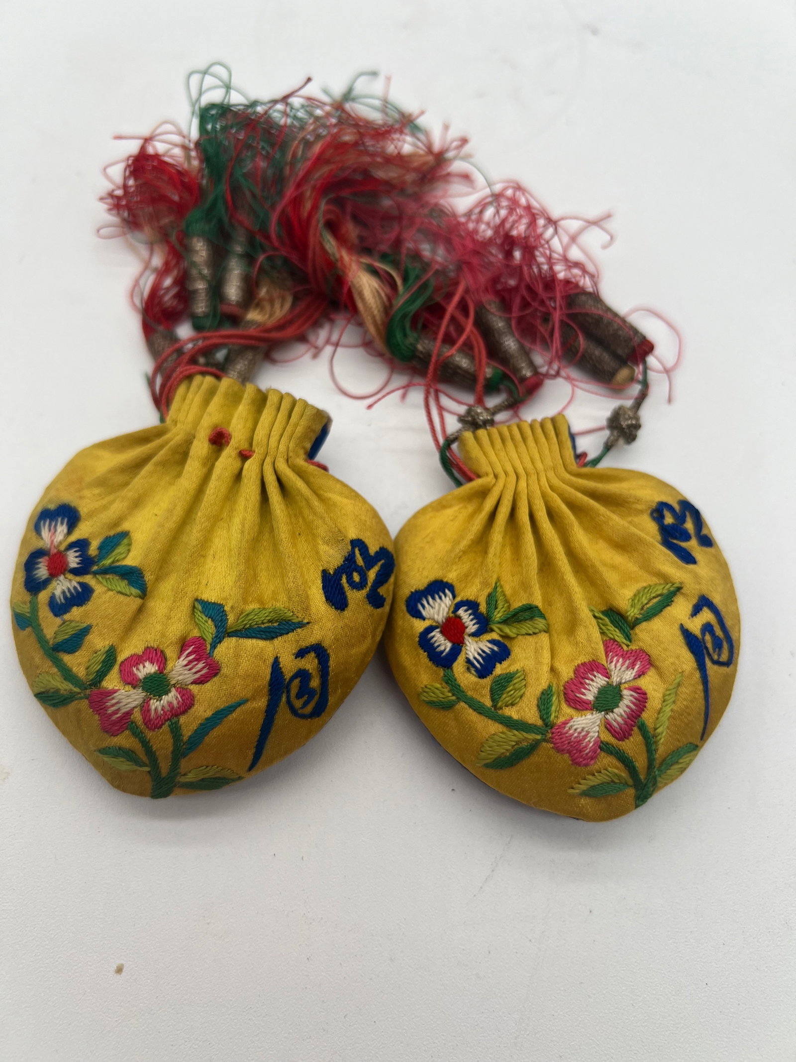 A pair of Chinese silk embroidered purses, circa 1920: A pair of Chinese silk embroidered purses, circa 1920, one side in blue silk, the other yellow, embroidered in satin stitch and depicting flowers and peaches, and having draw string and tassels to the