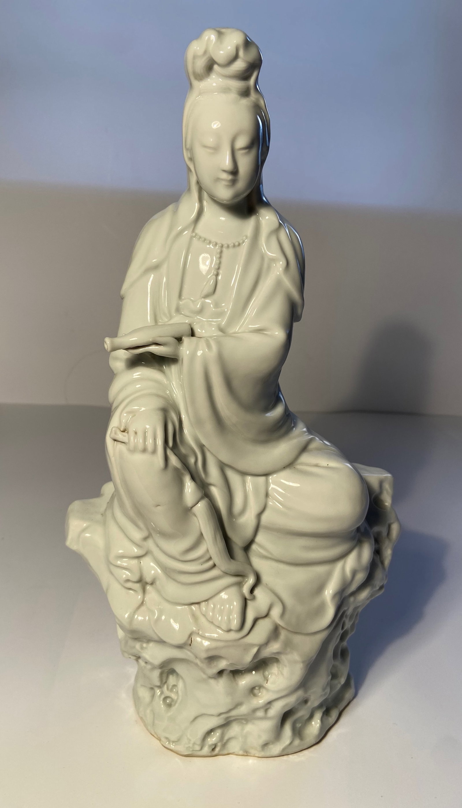 A Chinese Blank de Chine porcelain Kwan Yin statue: Qing dynasty (1644–1912);The statue you have shown is indeed a blanc de Chine figure of Guanyin (also known as Kuanyin or Kwan Yin), depicted sitting on a rock ; Height: 14.5 inches
