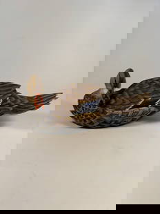 A carved duck decoy with reticulated carved wings by C. BURNS, Signed and dated " C Burn 88": The decoy features intricately textured feathers, naturalistic coloration, and a striking iridescent blue speculum on each wing. The bird is presented in a relaxed, turned-head pose, showcasing except
