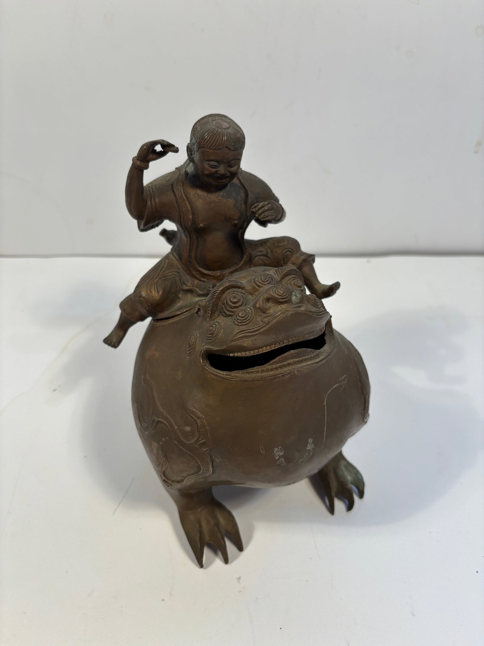 A Chinese bronze incense burner: Late 19th to early 20th, The figure riding the beast appears to be a Buddhist or Daoist child deity, possibly Sudhana. Height: 8 inches.