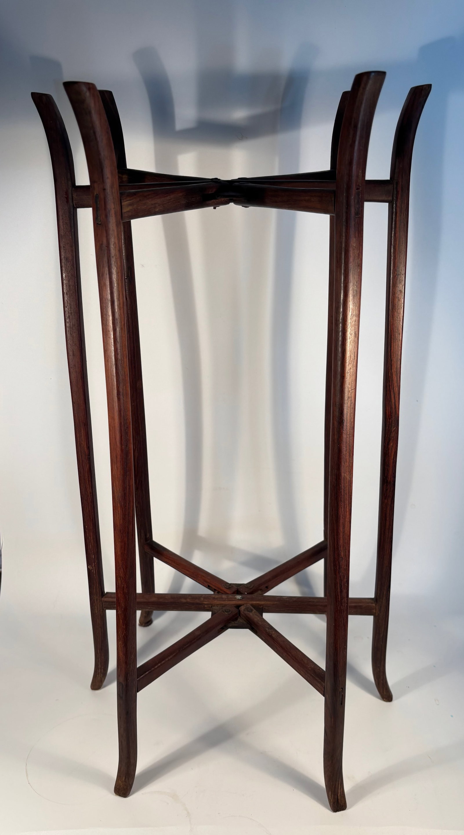 A Chinese huanghuali/ rosewood six- leg folding wooden stand: Qing Dynasty (1644-1912); Its elegant curved legs, cross-stretcher construction, and hinged joints . Height: 27.5 inches; Diameter: 14 inches. ,