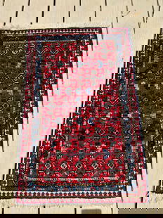 A Persian Qashqai 100% wool Rug, Southwest Iran: Probably Early 20th Century; A hand-knotted Qashqai tribal rug, early 20th century, from southwest Iran. The deep red field is filled with an array of repeating diamond and floral motifs, framed by mu