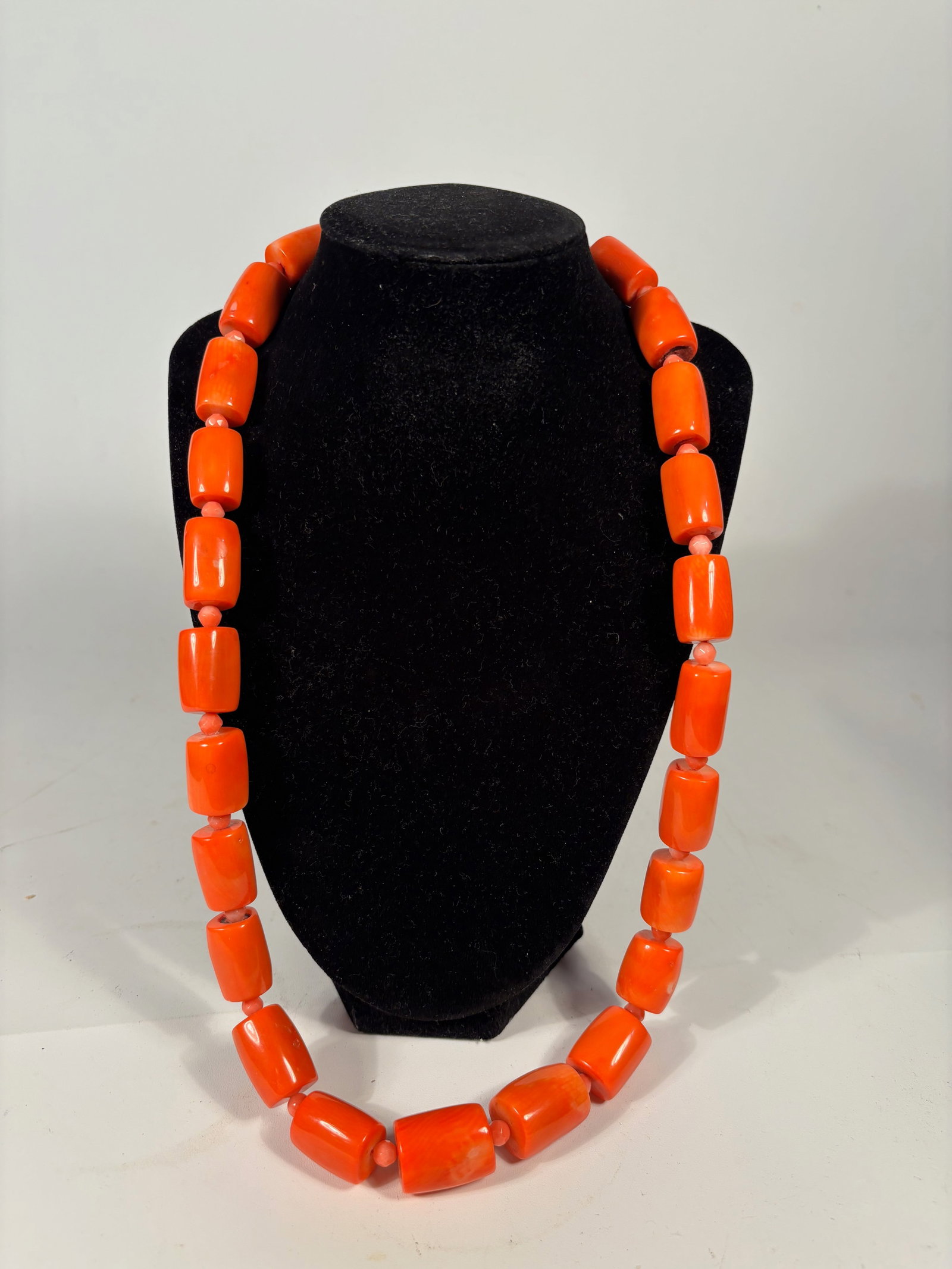 A Mediterranean Red Coral Bead Necklace: A striking necklace composed of natural Mediterranean red coral beads, featuring 29 cylindrical to barrel-shaped coral beads, interspersed with smaller spacer beads. The coral displays rich reddish-or