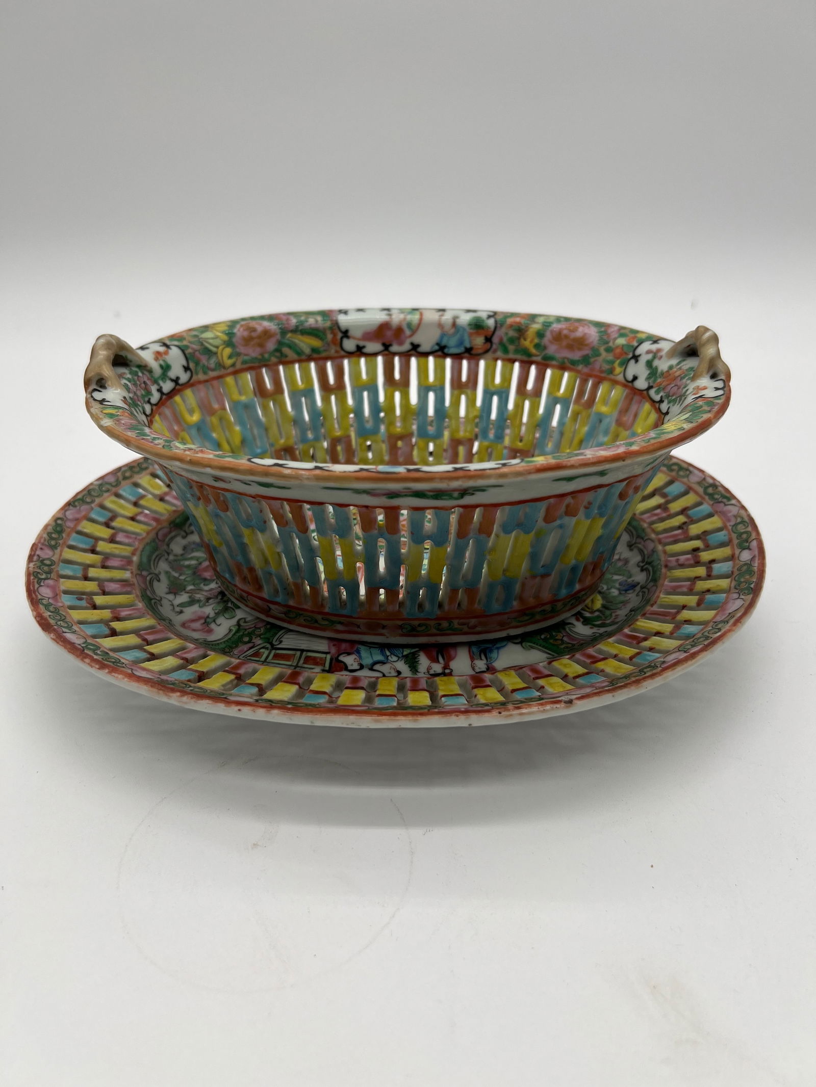 A set of Chinese Famille Rose reticulated porcelain basket and plate: Qing Dynasty (1644-1912); This set has a detailed, colorful enamel decoration, with what looks like a combination of floral and geometric patterns around both the basket and the plate. The handles on