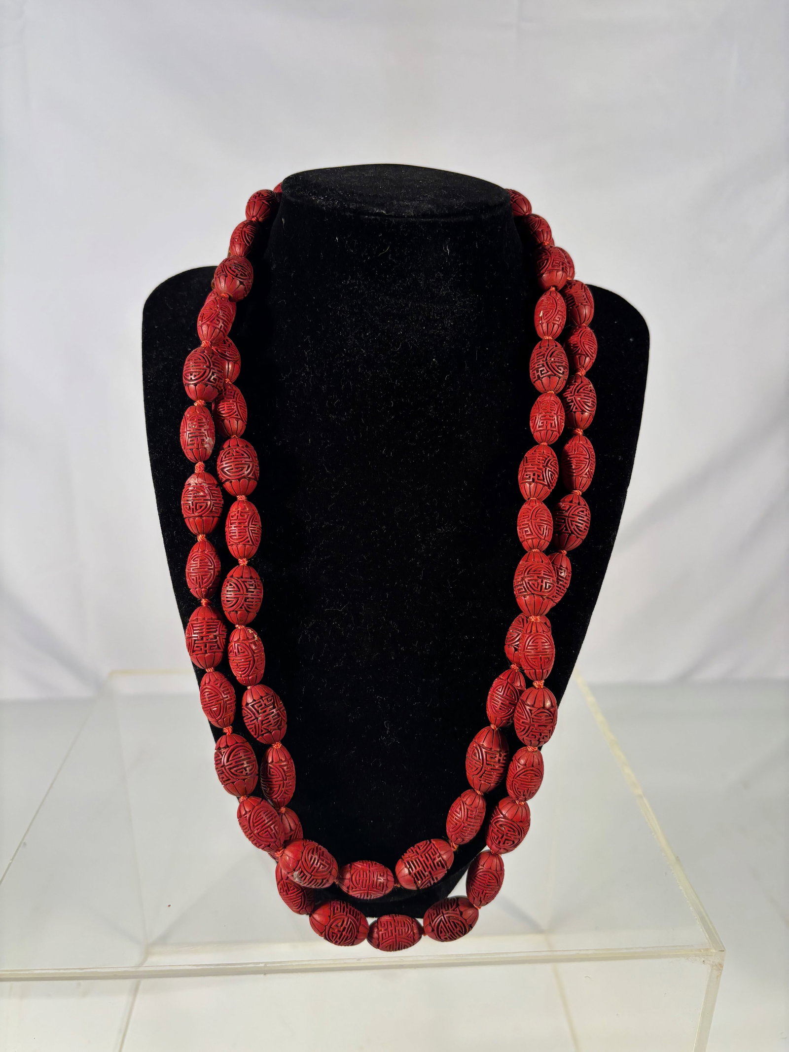 A Chinese Carved Cinnabar Lacquer Bead Necklace: Qing Dynasty(1644-1912); A finely crafted necklace comprising hand-carved cinnabar lacquer beads, each intricately incised with geometric and floral motifs. The beads are strung on cord with small spa