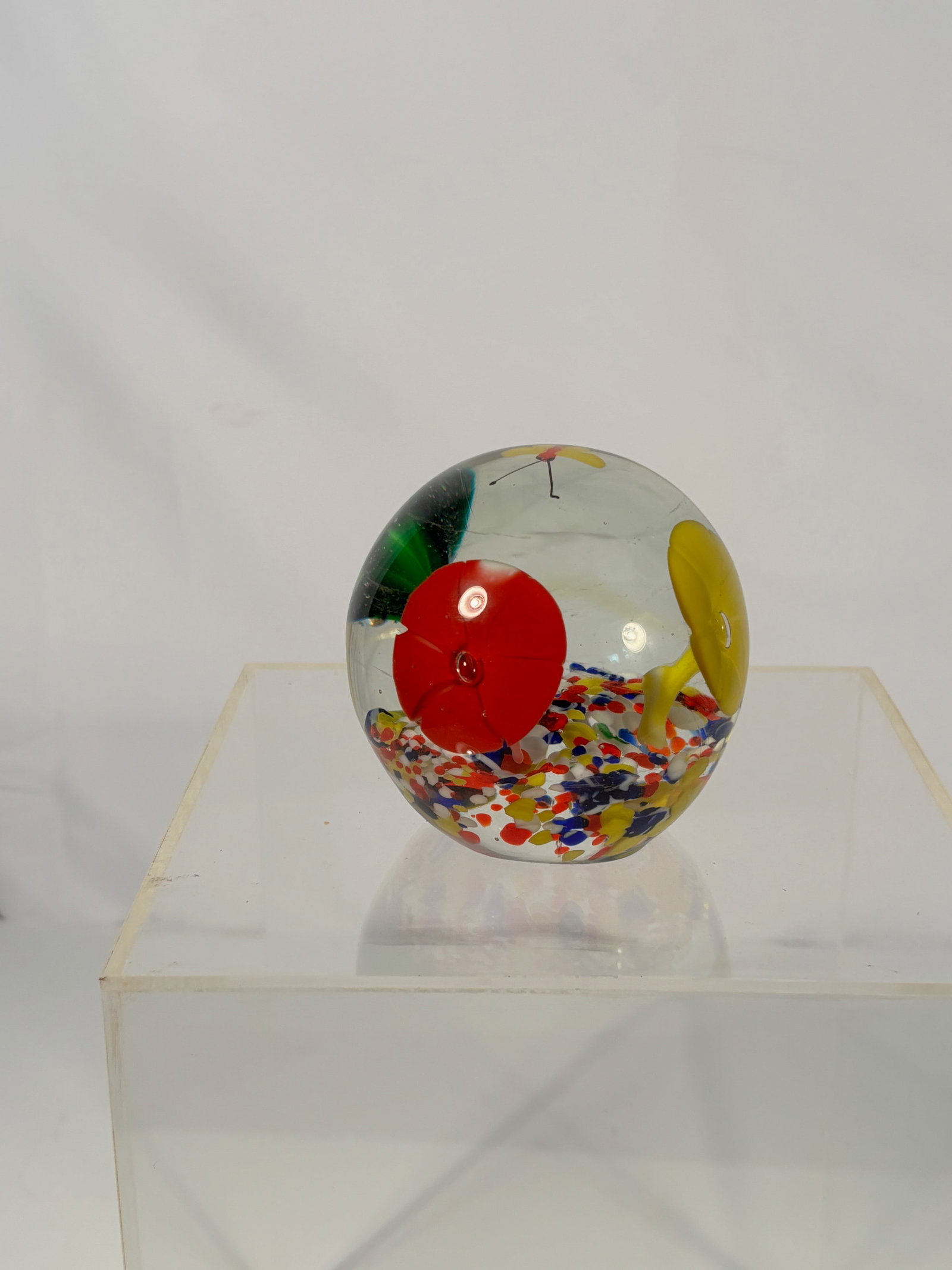 Murano Style Art Glass Paperweight with Lampwork Flowers and Butterfly, Millefiori Ground: A clear spherical art glass paperweight featuring an internal garden composition with multicolored millefiori-style base and lampwork floral elements in red, yellow, and green, along with a yellow but