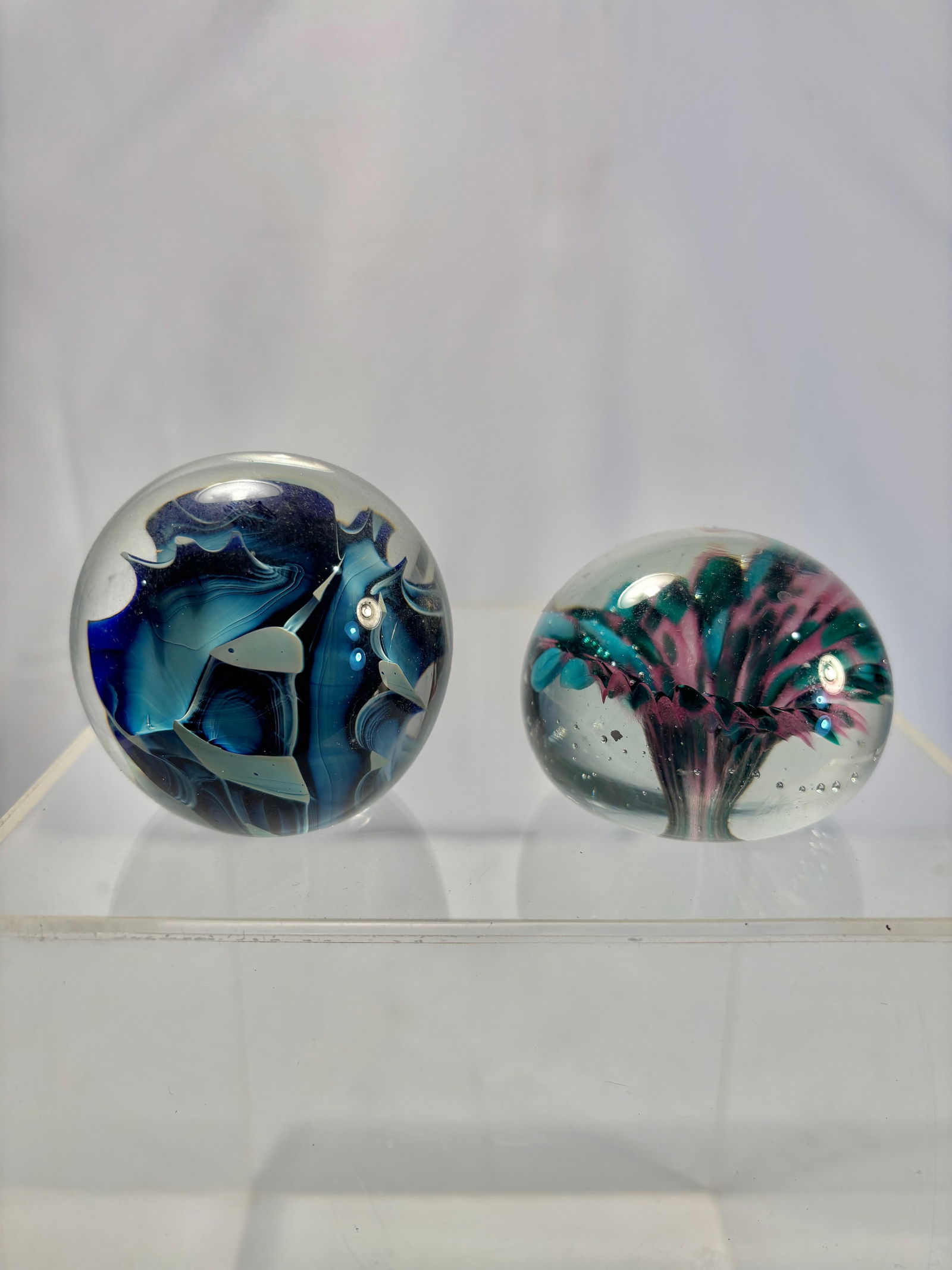 Lot of Two Studio Art Glass Paperweights, Abstract Floral & Swirl Designs: A group of two vintage studio art glass paperweights, each with vibrant internal sculptural designs. One features a pink, teal, and white swirling floral burst with controlled bubbles; the other displ