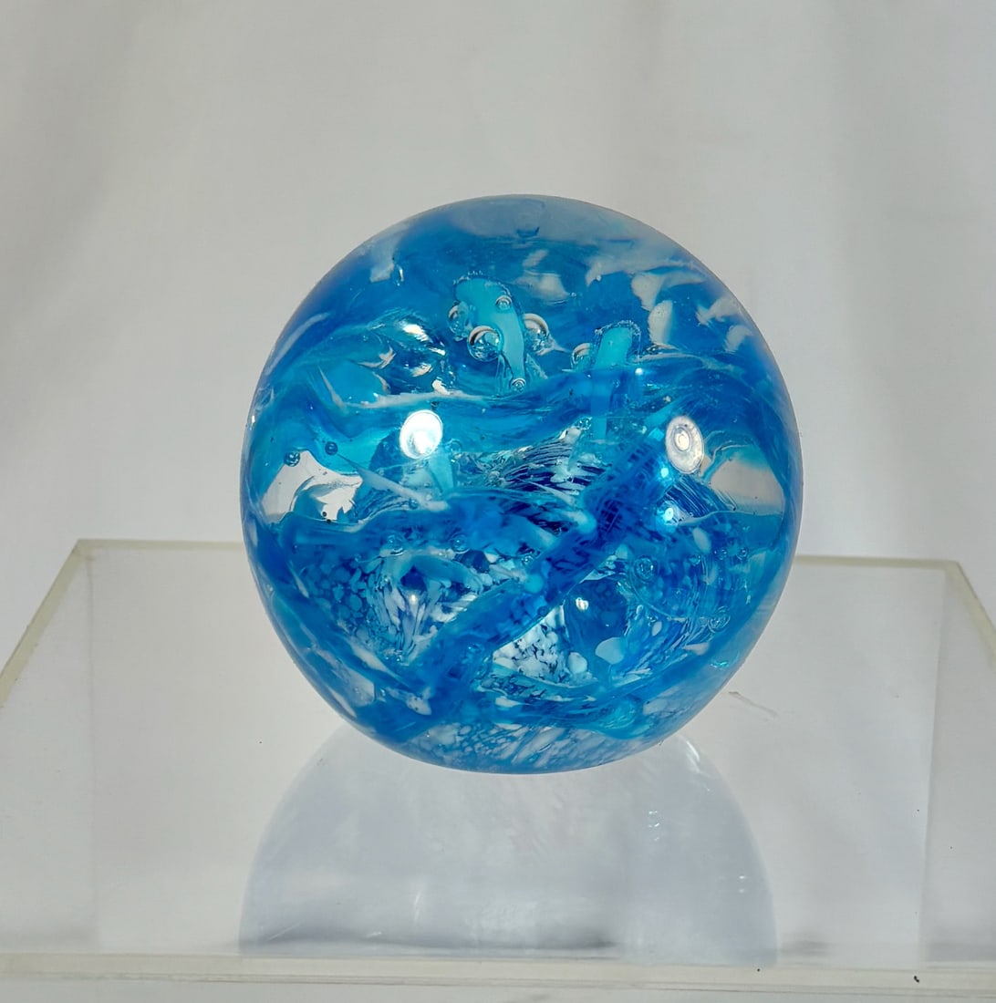A Hand-Blown Blue Art Glass Paperweight: A vibrant hand-blown art glass paperweight featuring swirling shades of blue and white with bubble inclusions throughout. The internal design resembles ocean waves or a stormy whirlpool, demonstrating