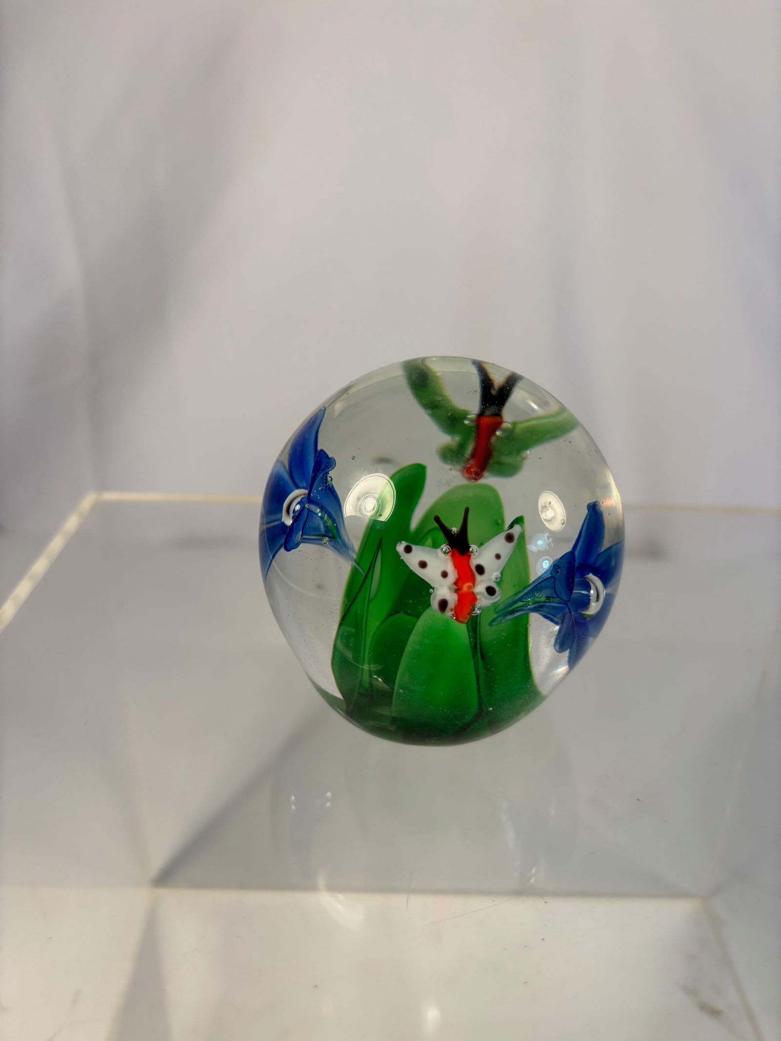 Lampwork Glass Paperweight with Butterfly and Blue Morning Glory Flowers: A fine clear glass paperweight featuring a detailed red-and-white butterfly among green foliage and two cobalt blue morning glory blossoms, rendered in lampwork technique. Dimensions?Diameter: 2.75 in