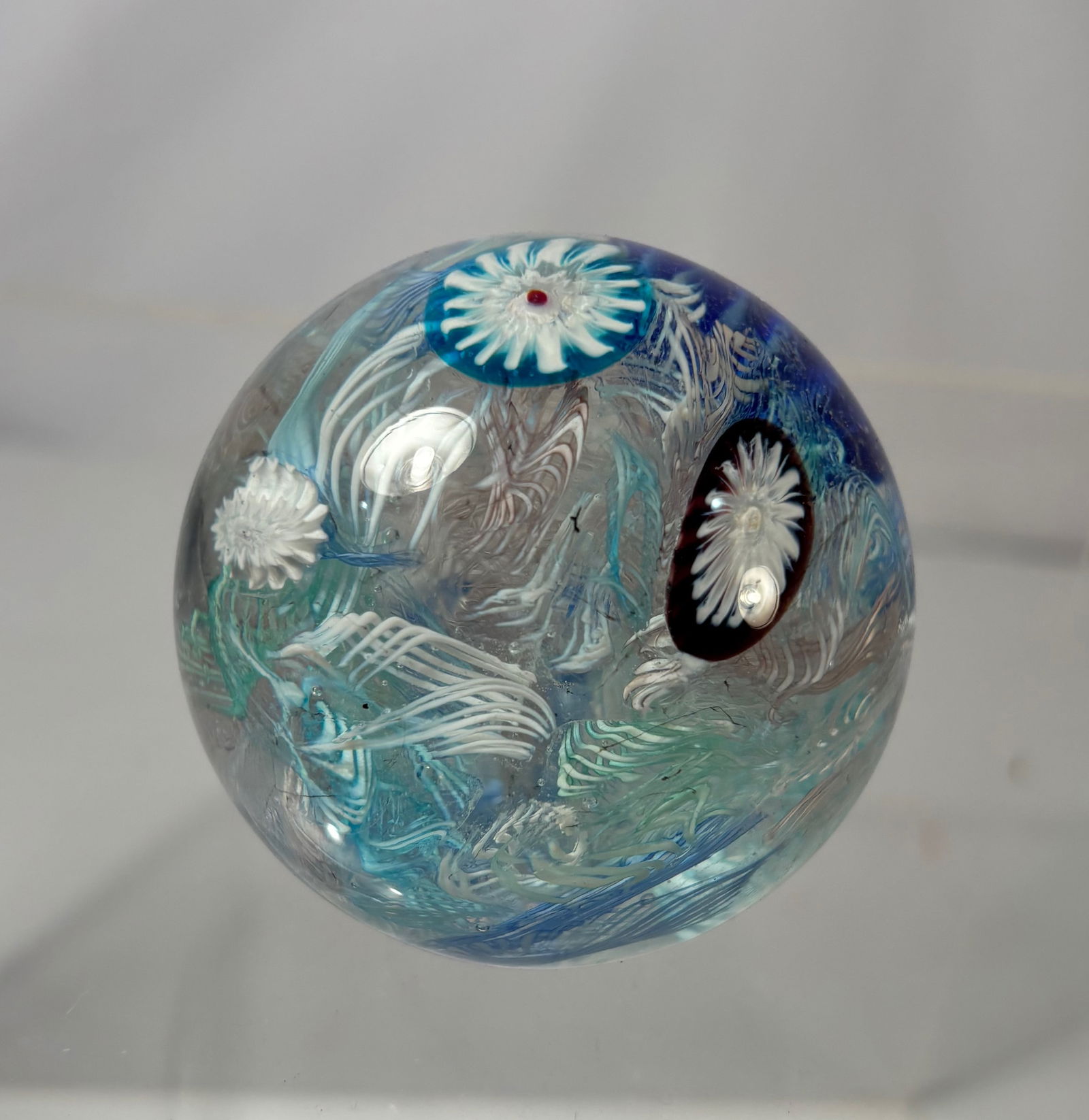 Murano Art Glass Paperweight, Blue Swirl with Floral Millefiori, Italy: Murano art glass paperweight, Italy, featuring blue and aqua swirled glass with embedded white floral millefiori canes and flowing internal ribbon decoration. The spherical form displays good clarity