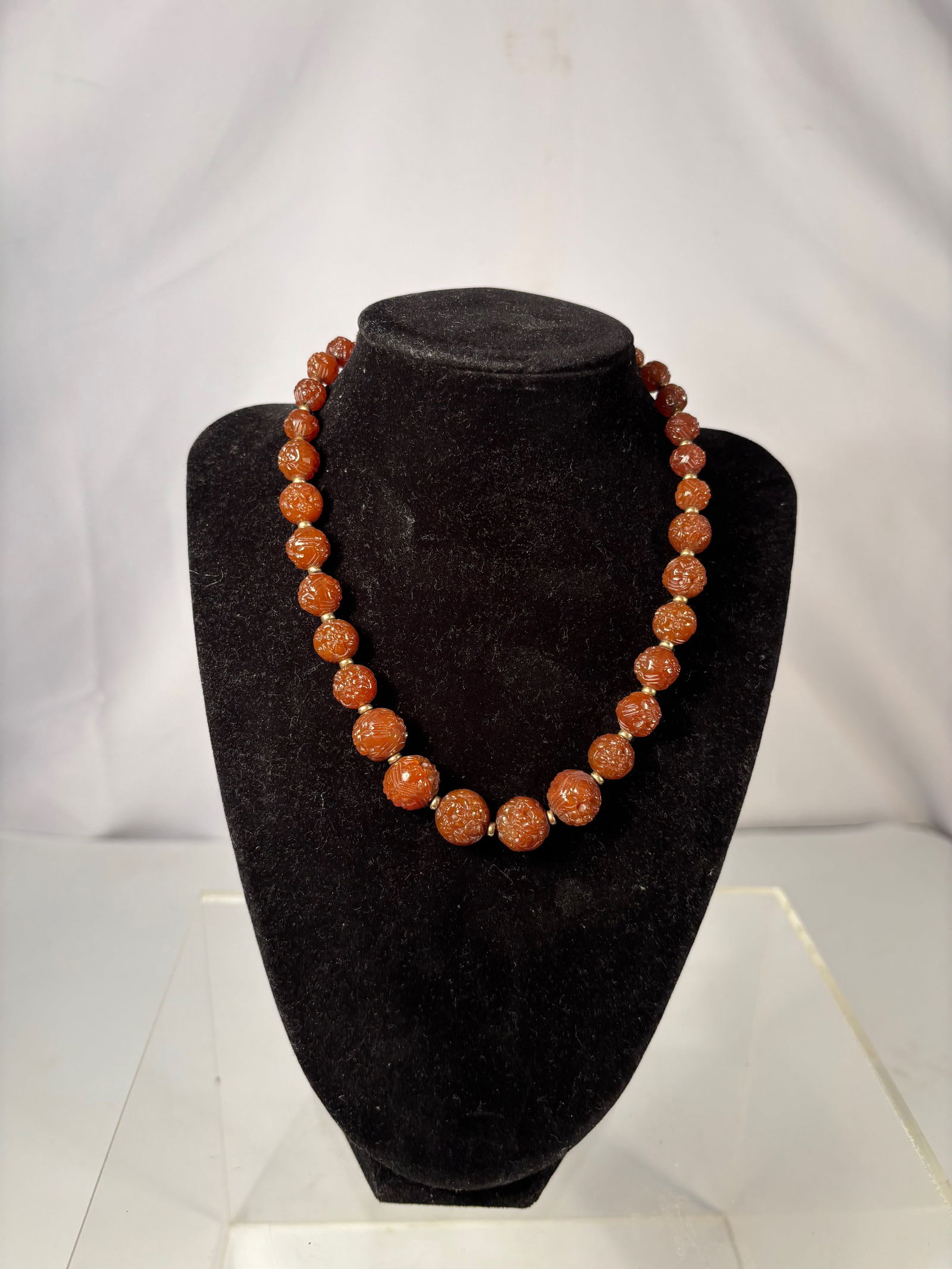 A Carved Carnelian Bead Necklace with Gold-Tone Spacers: This necklace is composed of carved reddish-brown carnelian or agate beads, each decorated with repeating floral and scroll motifs. The beads display attractive translucency and natural color variatio