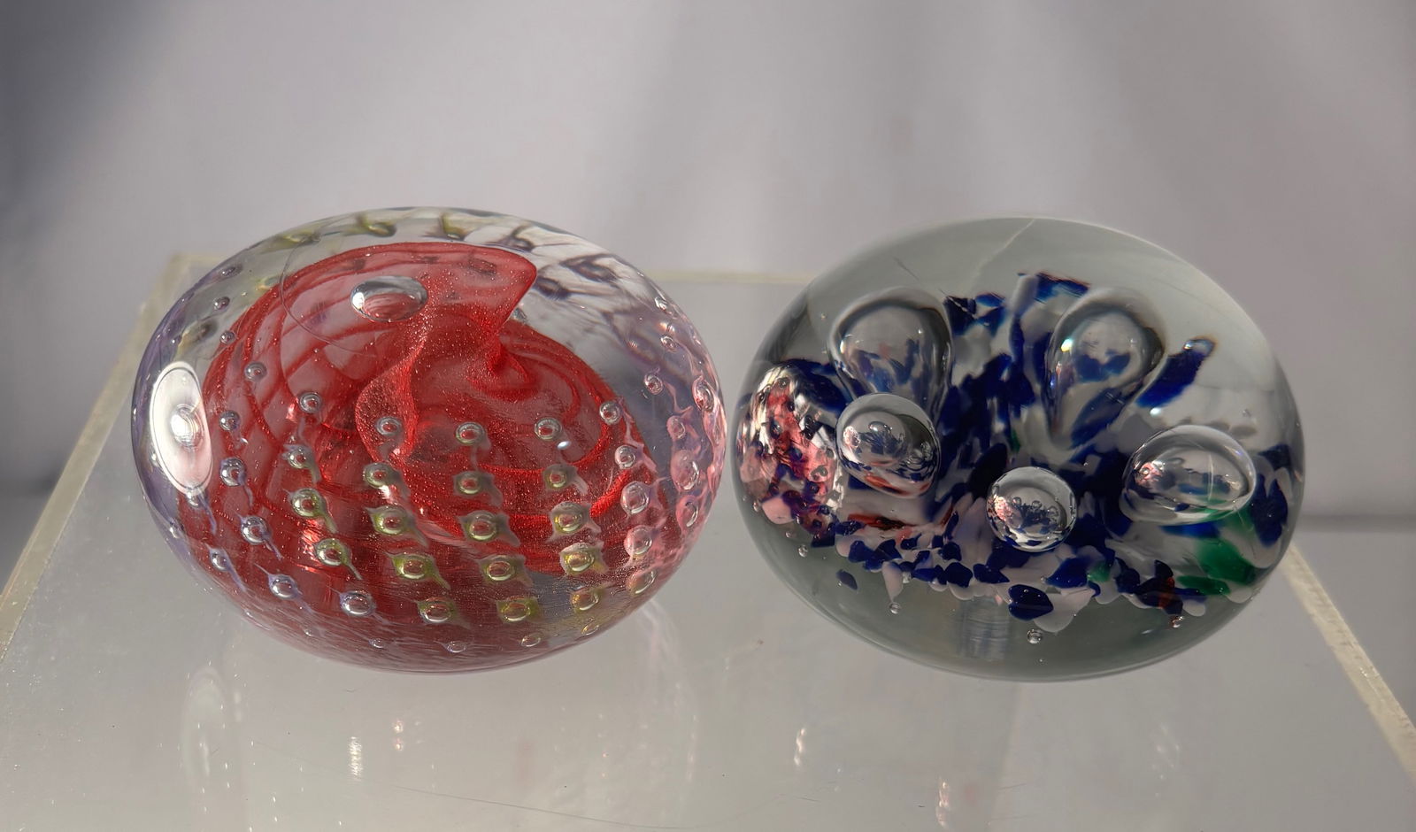 Pair of Studio Art Glass Paperweights, One Signed Gibson: A pair of studio art glass paperweights, each featuring a distinct internal abstract composition encased in clear glass. One example is signed Gibson and displays a dynamic red swirling form accented