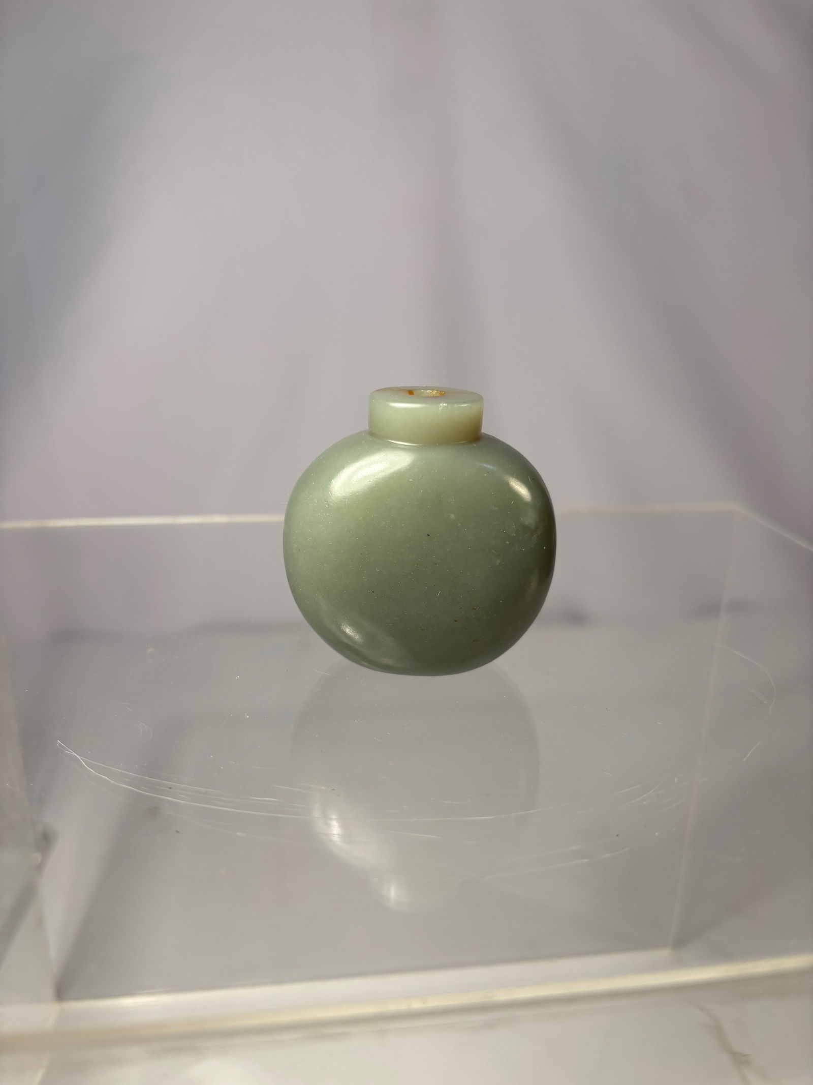 A Chinese celadon jade Snuff Bottle: Qing dynasty(1644-1912) ; Rendered from a softly toned celadon jade, this snuff bottle is carved in a rounded, flattened form with smooth, gently sloping shoulders rising to a short cylindrical neck.