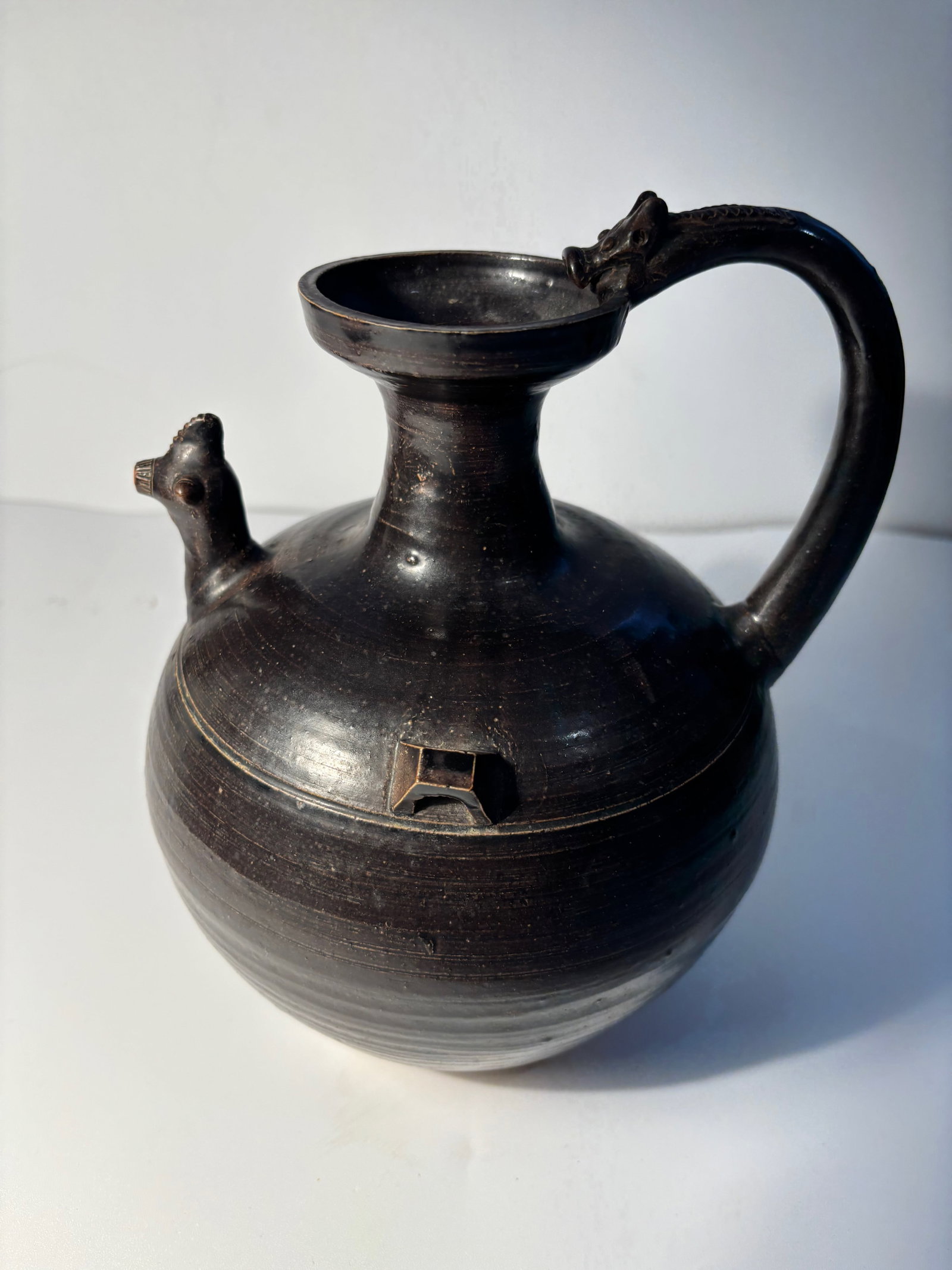 A CHINESE DARK BROWN-GLAZED POTTERY CHICKEN-HEAD EWER: JIN SIX DYNASTIES (4TH 5TH CENTURY),globular with cupped cylindrical neck, loop handle, chicken-headed spout.Provenance: From an prominent Midwest family collection in US.Dimensions?