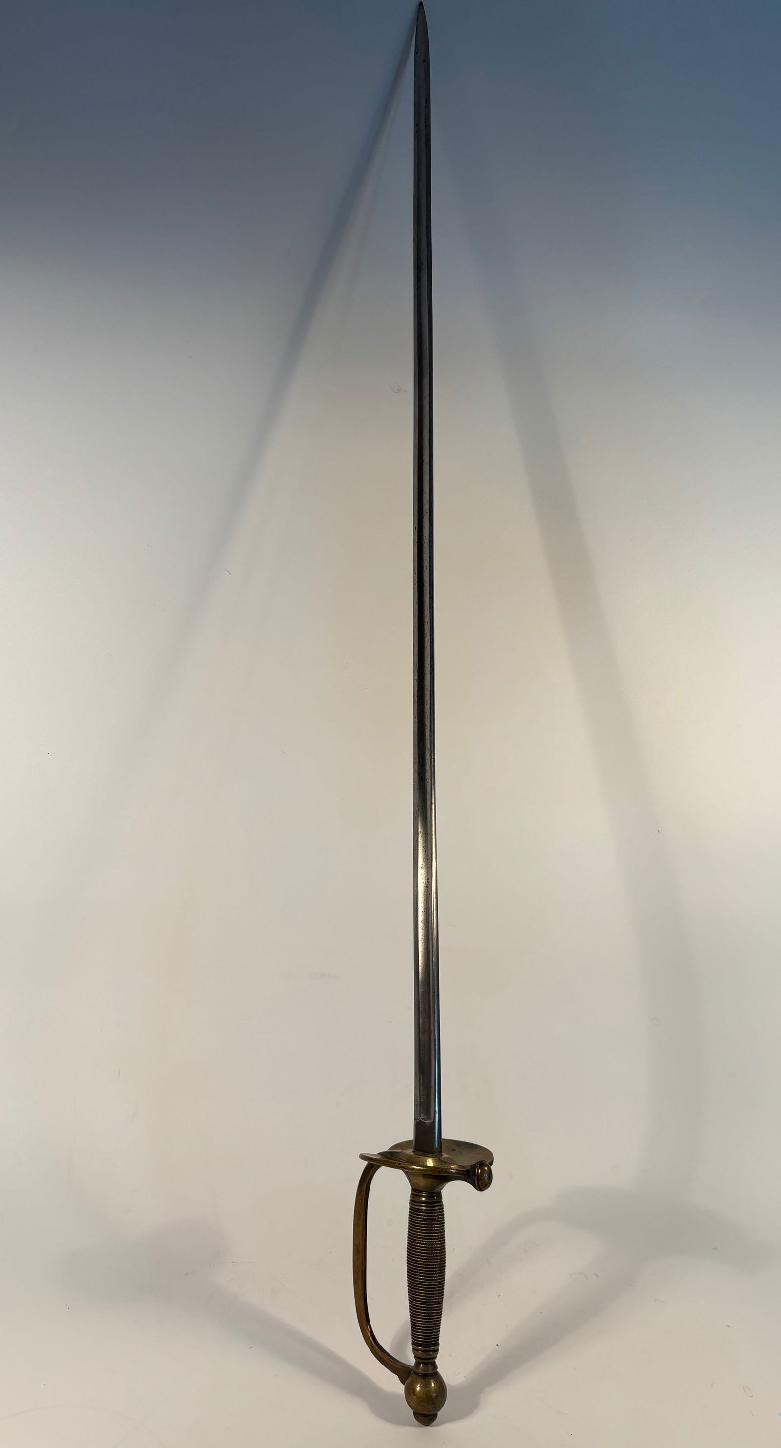 Officer’s Dress Sword with Brass Hilt and Wire-Wrapped Grip: Early 19th Century; Blade: Slim, straight, primarily designed for thrusting—not combat but ceremonial/military attire use; Hilt: Brass D-guard with a knuckle bow. Grip: Wire-wrapped (usually over a