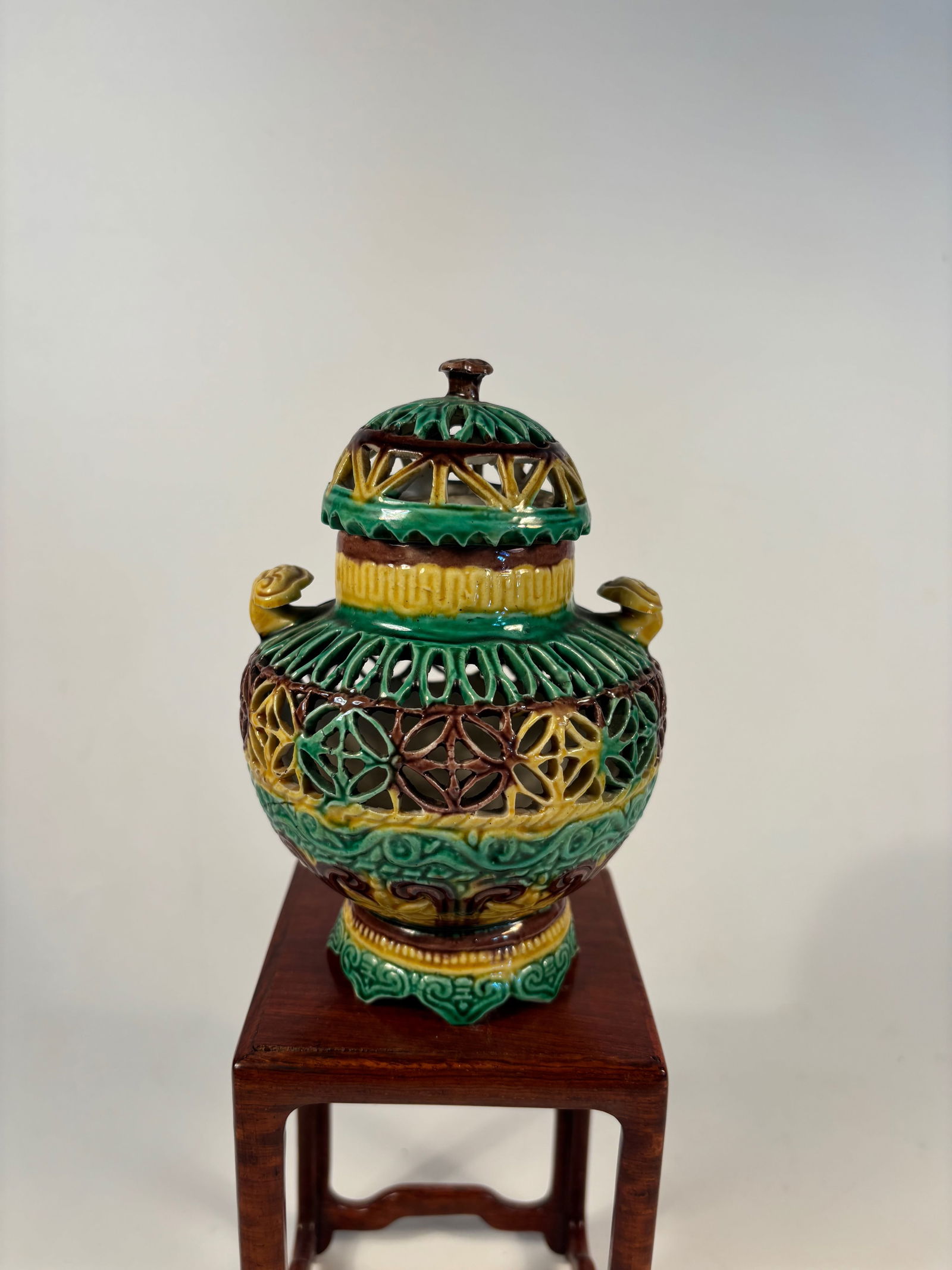 A Chinese sancai-glazed pierced porcelain incense burner: Qing Dynasty (1644-1912); Three-color” glaze (green, yellow, brown) typical of Tang-style revival ware; Intricate pierced lattice work on both body and lid; Small stylized animal head or