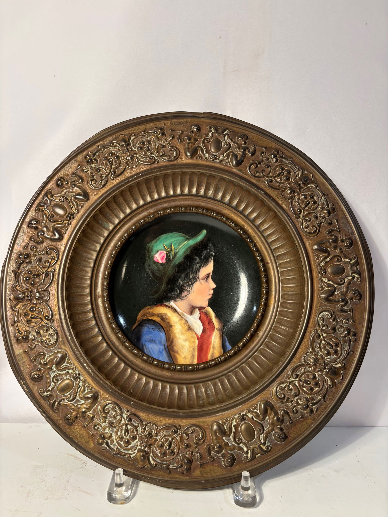 An European Porcelain Portrait Plaque of a Child in Gilt Bronze Tondo Frame, Late 19th Century: Hand-painted European porcelain portrait plaque depicting a young child in period costume, shown in profile against a dark ground. The finely painted plaque is set within an ornate gilt bronze tondo