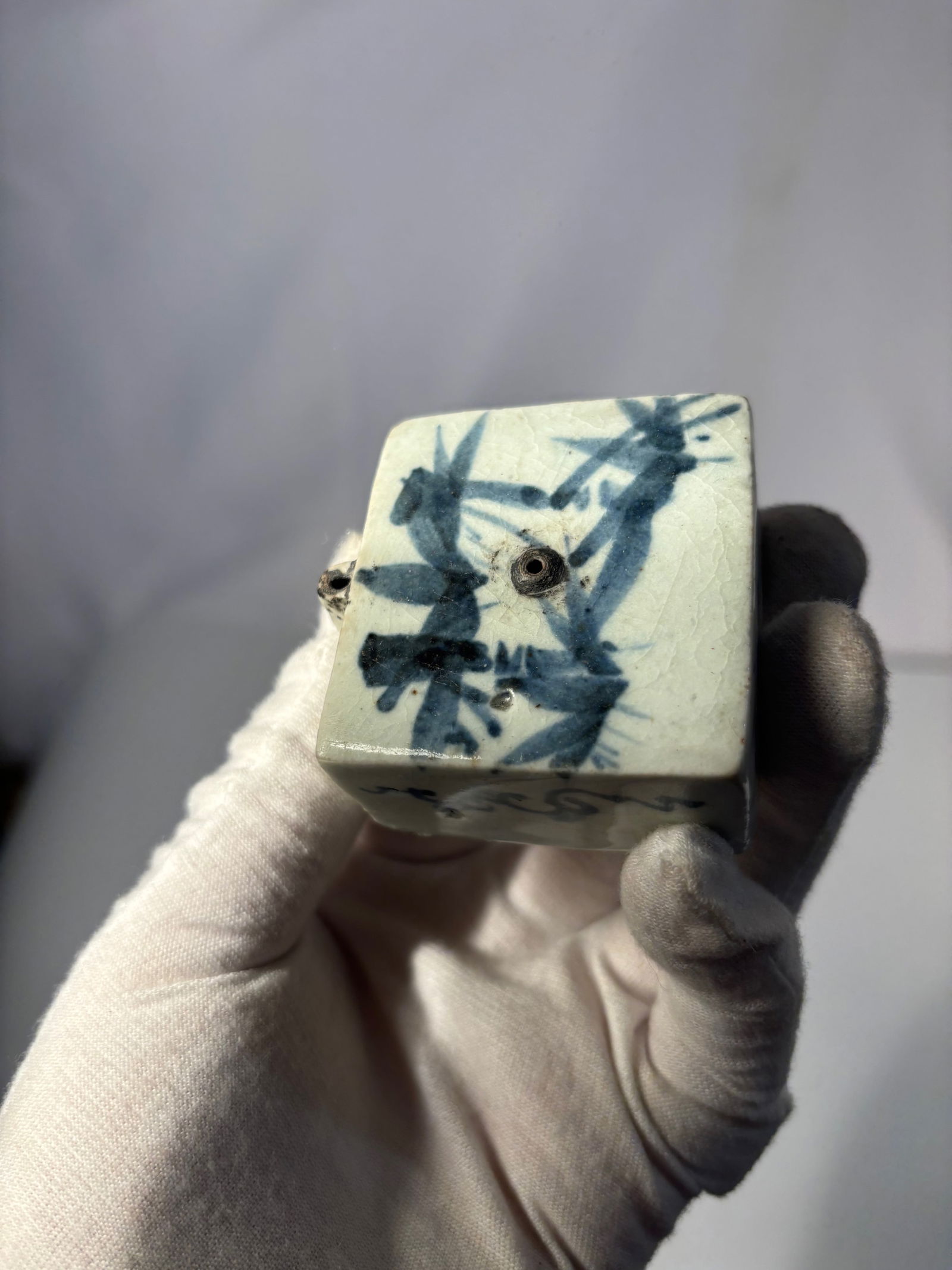 A Japanese Blue and White Porcelain Water Dropper (Suiteki), Edo Period (Probably): A Japanese blue and white porcelain water dropper (suiteki), of rectangular form, decorated in underglaze cobalt blue with stylized landscape and abstract scroll motifs. The top features dual