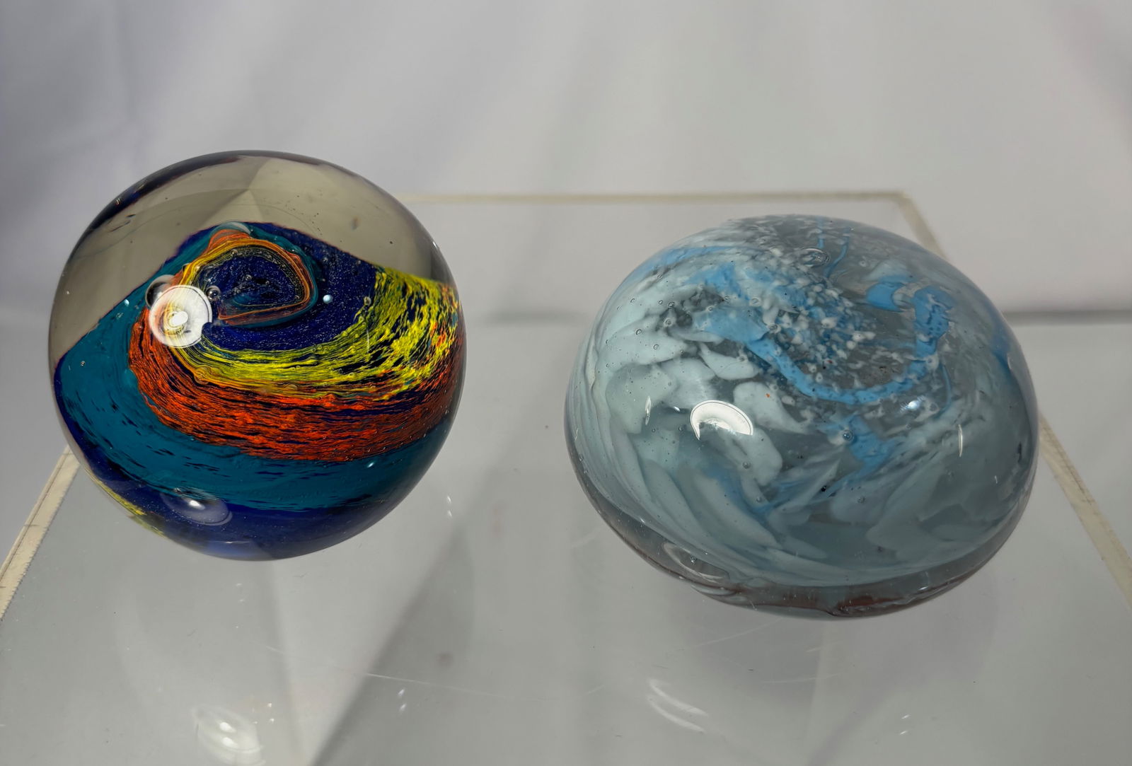 Set of 2 Studio Art Glass Paperweights, Abstract Swirl Designs: 2 studio art glass paperweights, each featuring a distinct internal abstract swirl composition encased in clear glass. One example displays a multicolored spiral with blue, yellow, and red tones creat