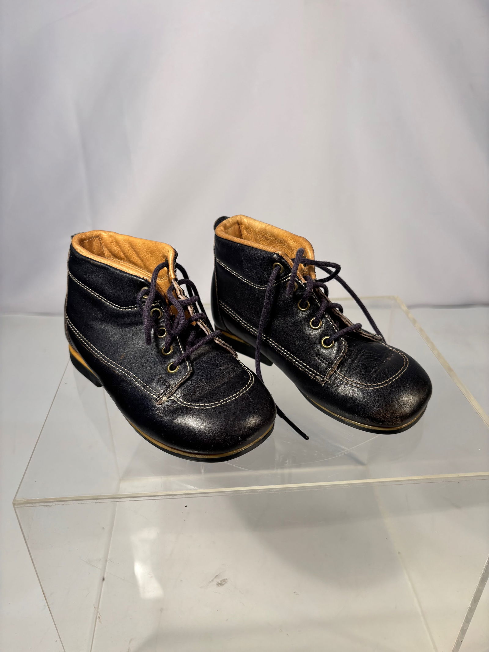 A Vintage Little Capezio Child’s Black Leather Lace-Up Boots, Early–Mid 20th Century: Vintage child’s lace-up boots by Little Capezio, crafted in black leather with contrasting white stitching and tan leather lining. The boots feature rounded toes, multi-eyelet lace fronts, and low s
