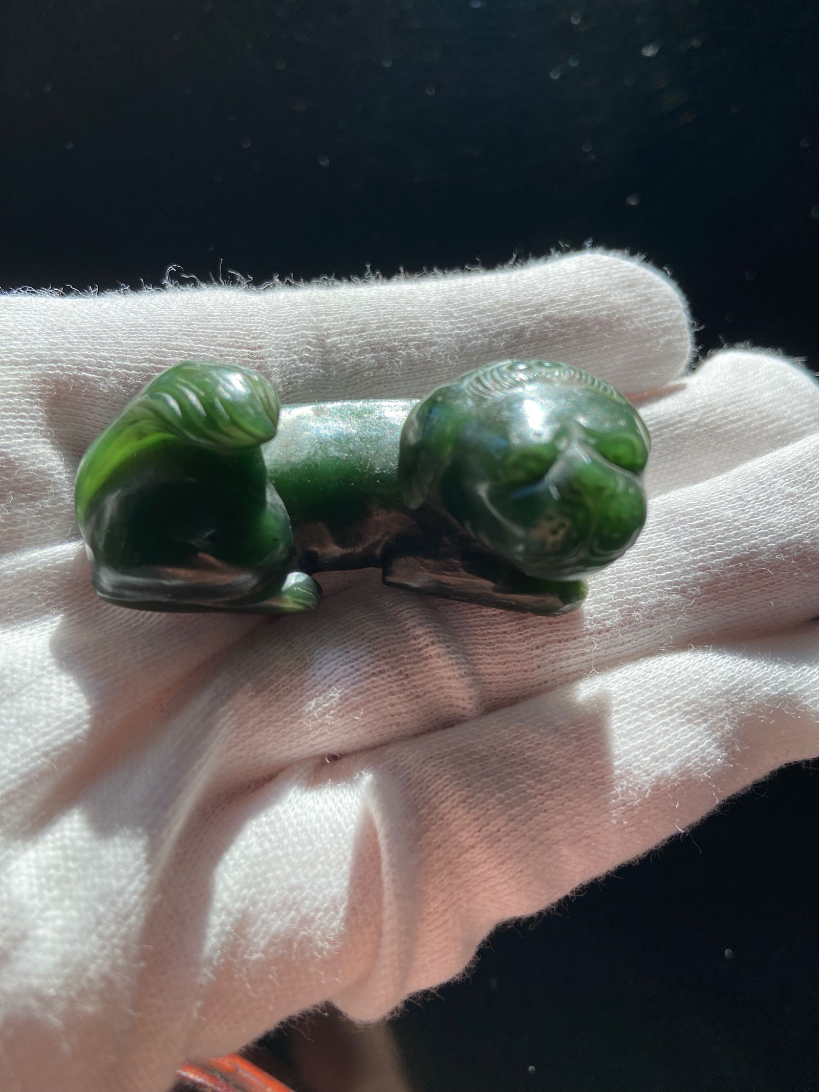 A Chinese green jade foo dog: 19th century, appears to be a carved jade or stone figure of a reclining animal, possibly a mythical creature or a dog, displayed on a wooden stand. Dimensions?LENGTH: 2 inches