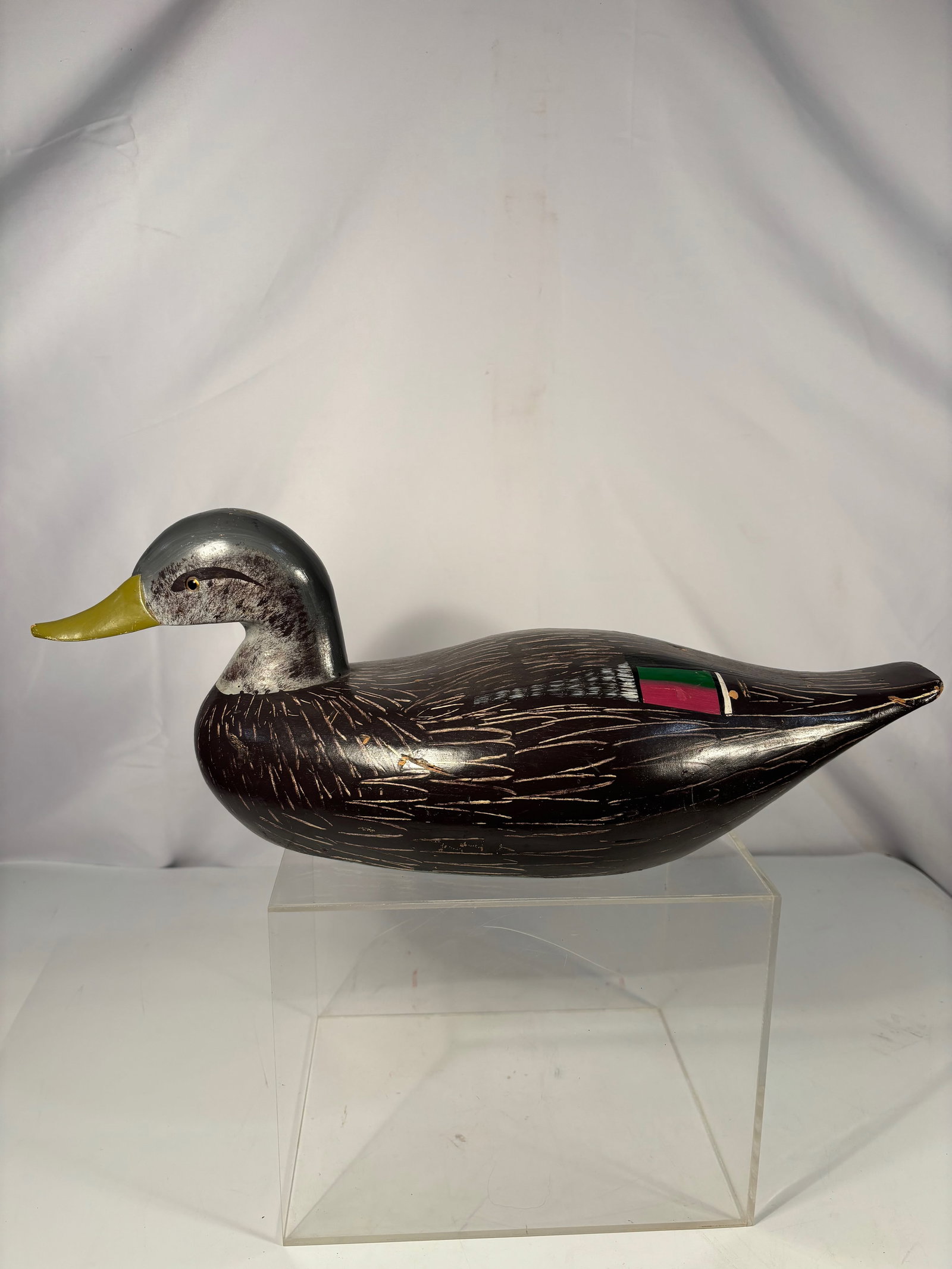 A Hand-Carved Duck Decoy with Incised Feather Detail, Mid-20th Century: Hand-carved wooden duck decoy with stylized form and finely incised feather detailing, featuring a painted surface with decorative coloration to the body. American folk art example, likely mid-20th