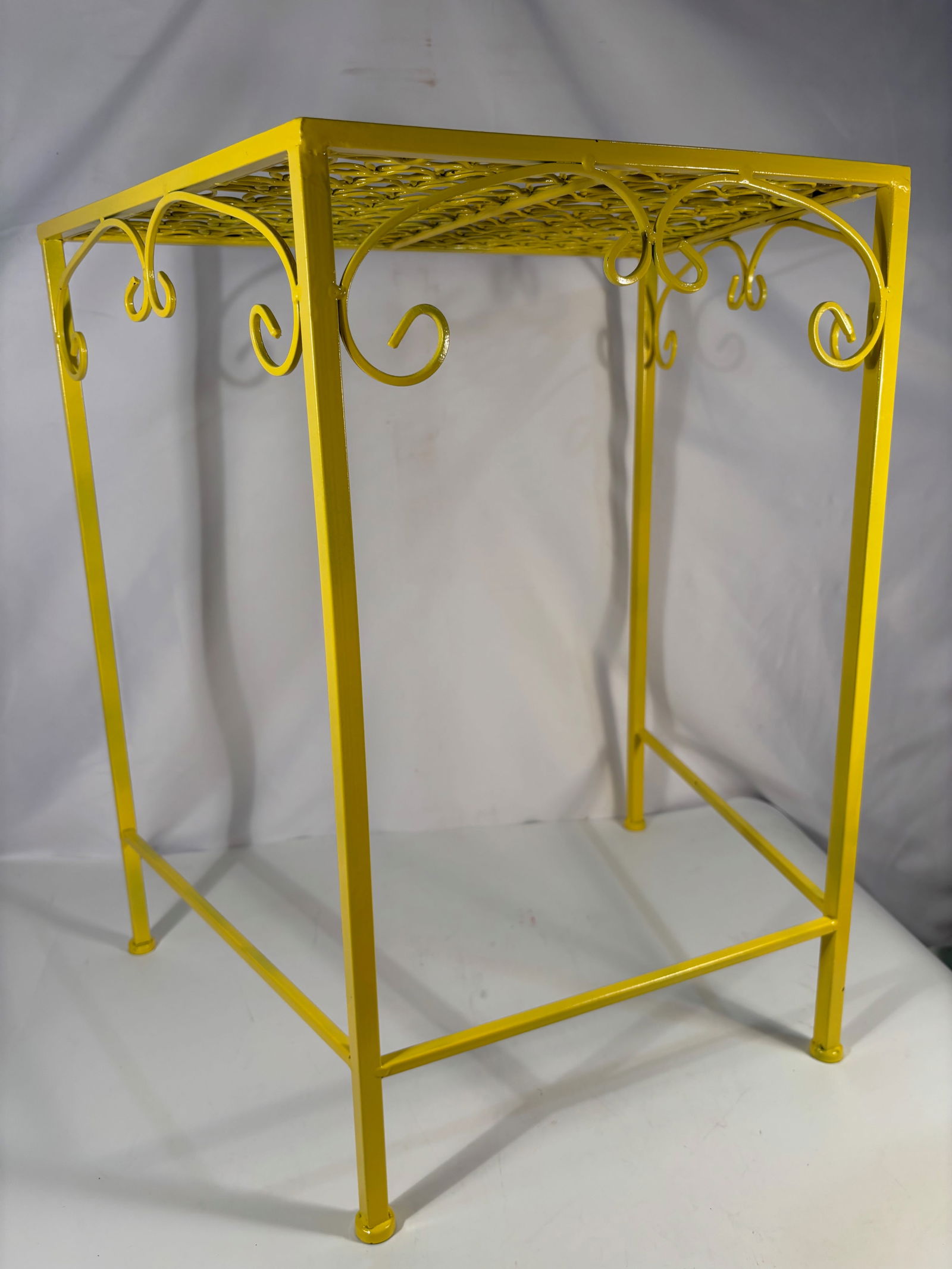 Vintage Yellow Painted Metal Plant Stand or Display Table: A vintage metal stand featuring an openwork lattice top with repeating geometric ring design, supported by slender legs with decorative scroll accents. Finished in a bright yellow painted surface,