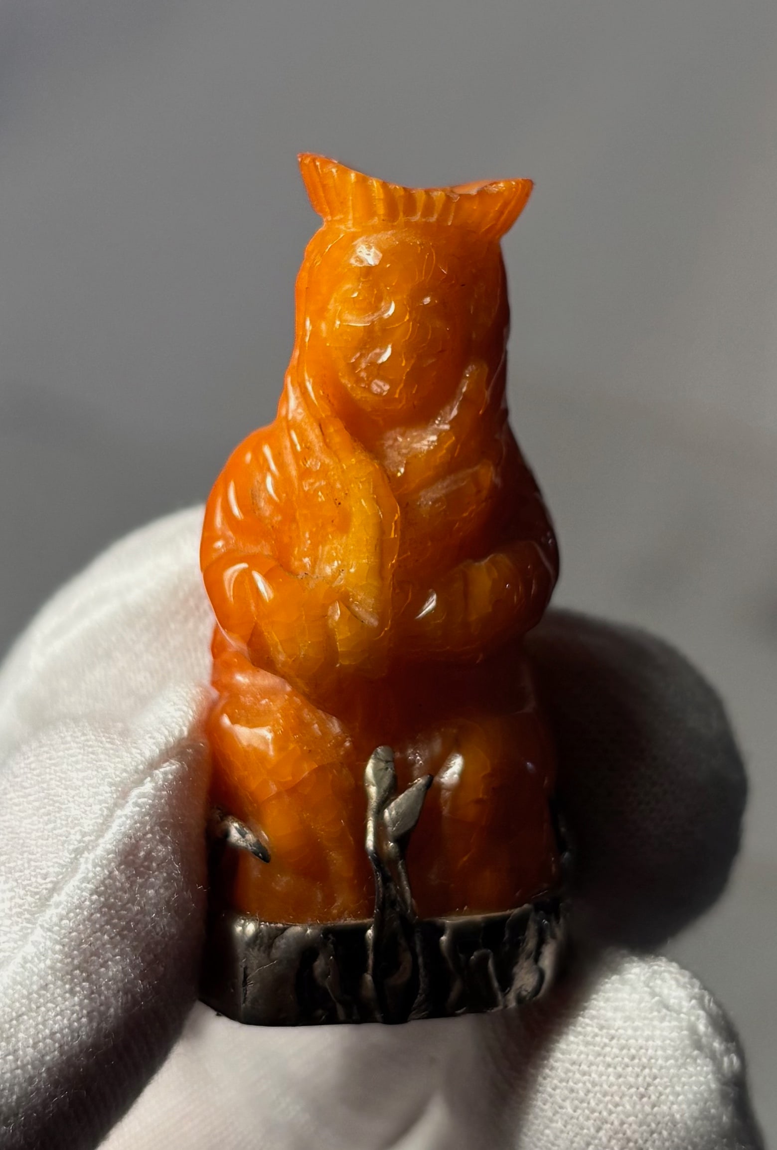 A Butterscotch Amber carved Figurine on Metal Base: Carved butterscotch amber bear figurine mounted on a textured metal base. The figure displays warm yellow-orange tones typical of butterscotch amber and depicts a seated bear with rounded features.Hei