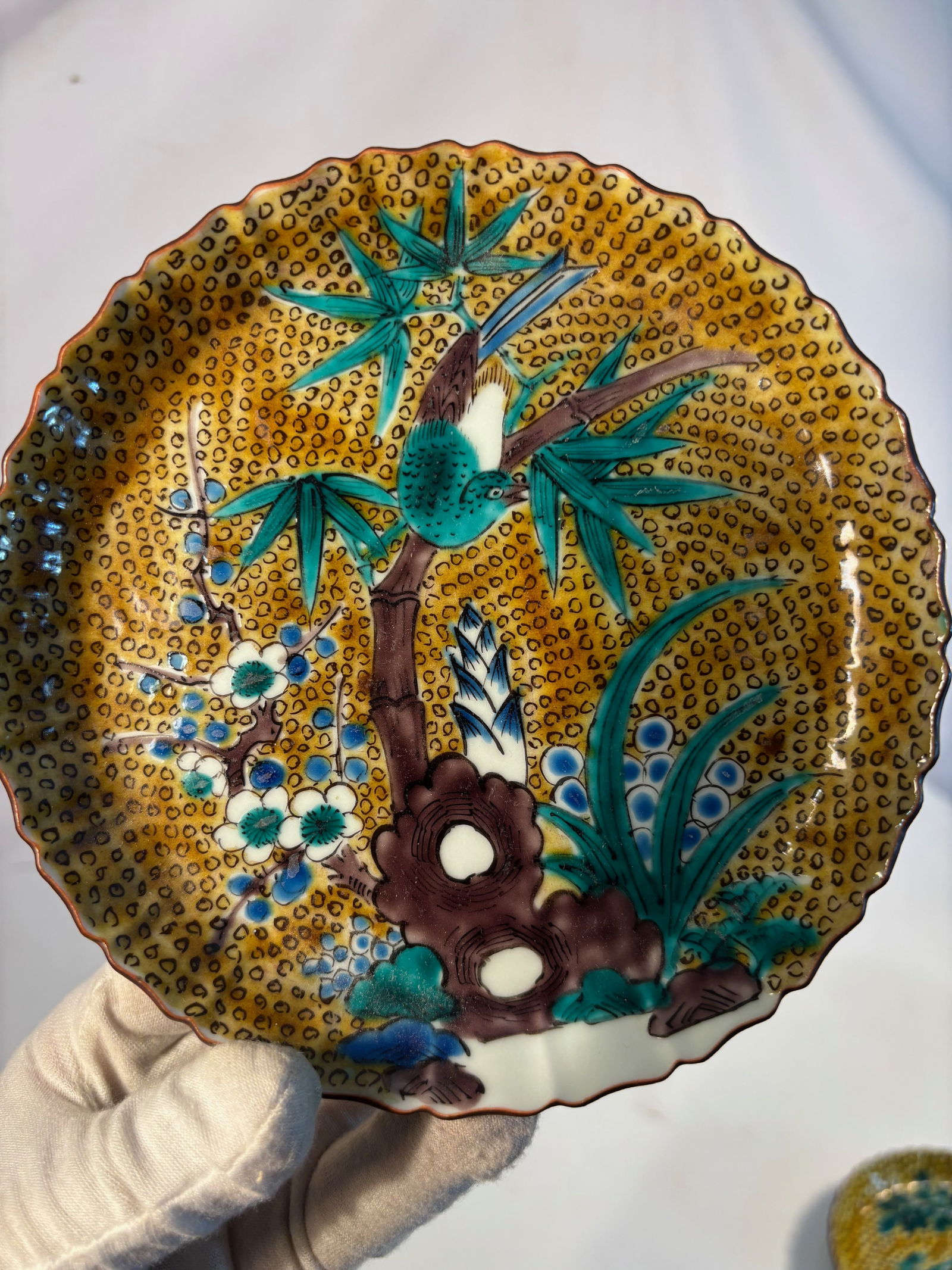 A Japanese Kokutani Lobed Dish, Meiji Period (1868–1912): Of lobed form, brightly decorated in the Kokutani palette of green, yellow, aubergine, blue, and white enamels, depicting a bird perched on a bamboo and prunus branch beside rocks, set against a dense