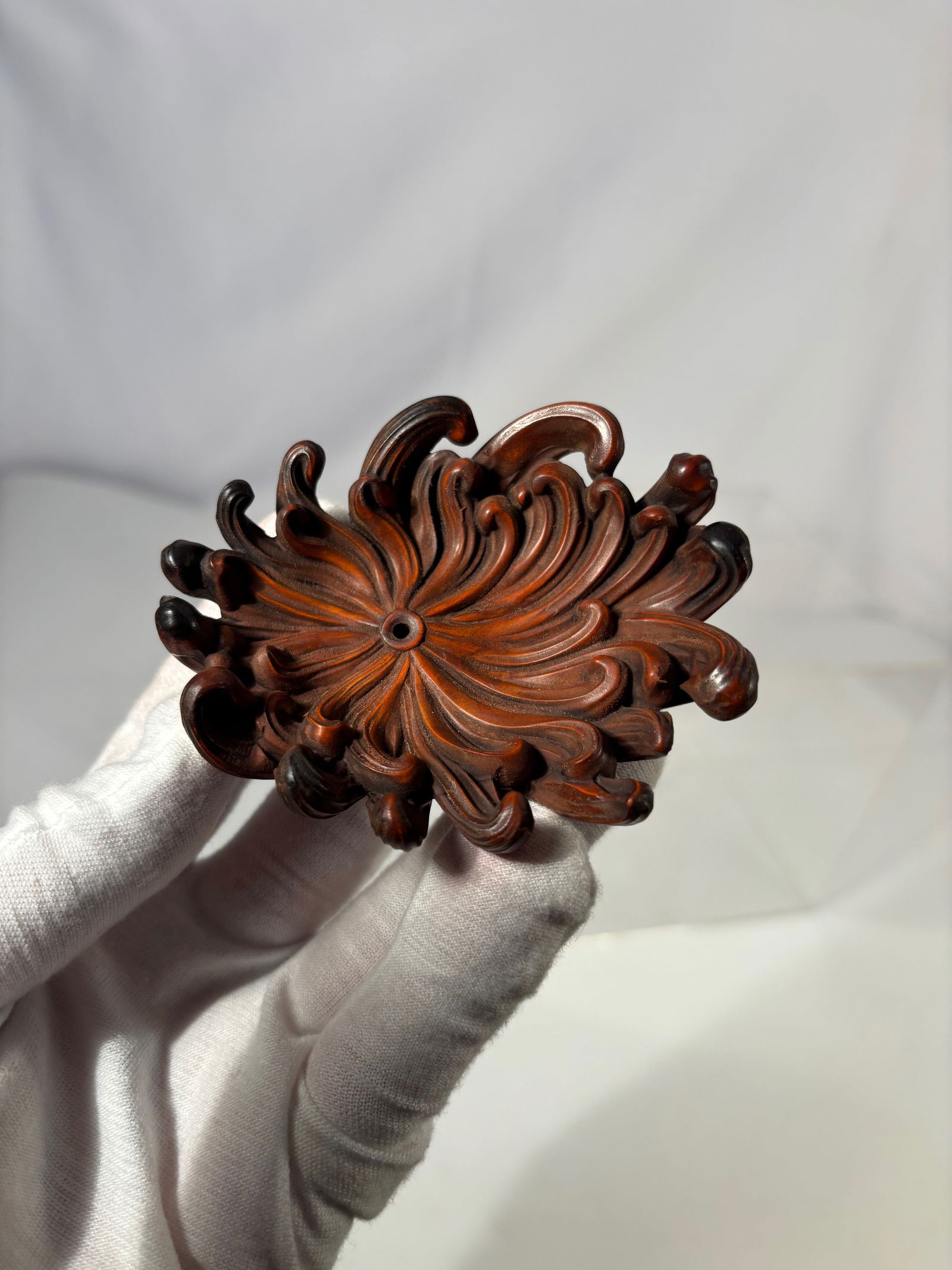 A Japanese Carved Wood Chrysanthemum Form Ornament: Japanese carved wood decorative ornament modeled in the form of a blooming chrysanthemum, with deeply carved, curling petals radiating from a central boss. Finished in a warm reddish-brown tone, empha