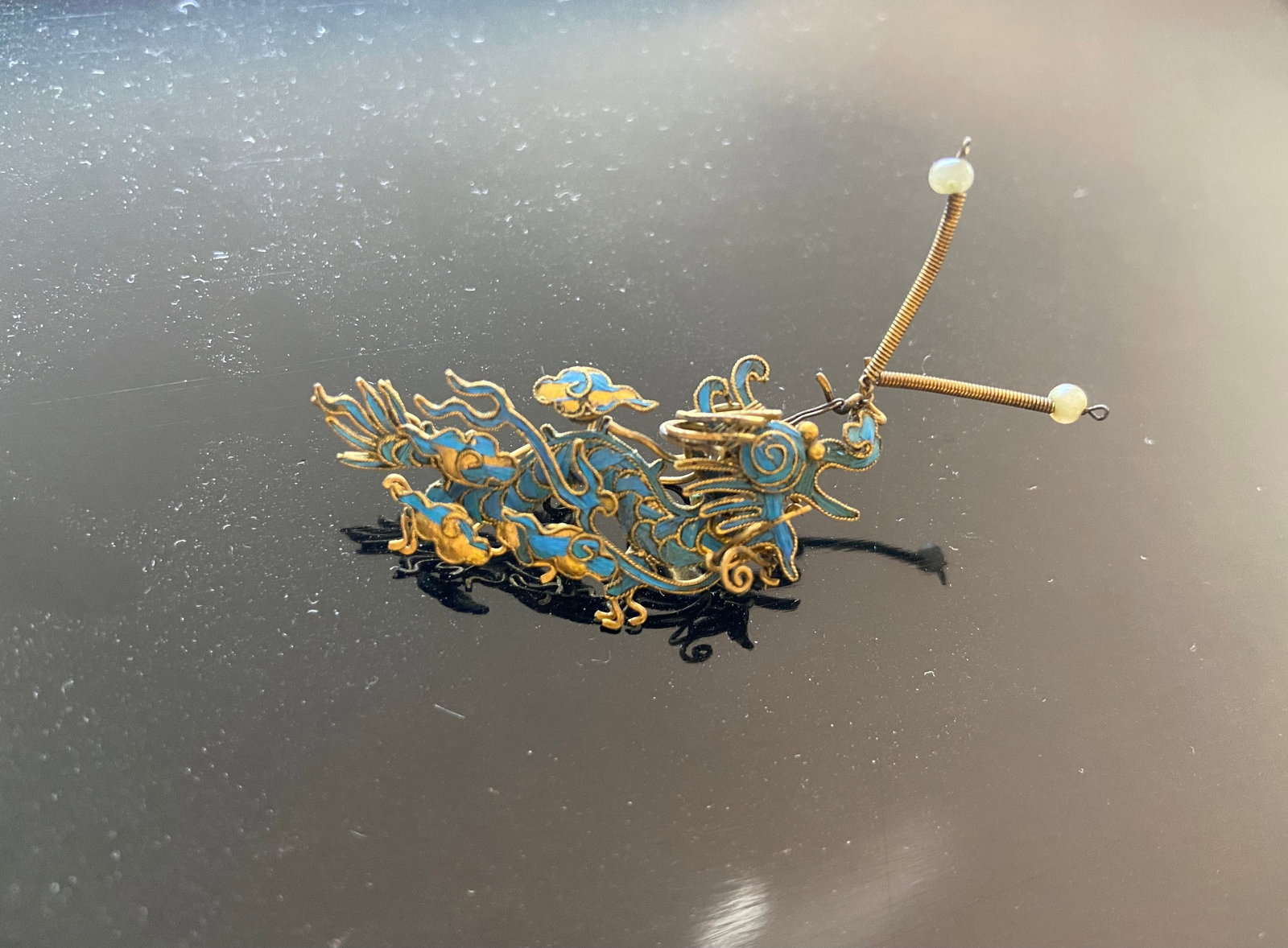 A Chinese Kingfisher feather gilt silver dragon style ornament: Qing Dynasty (1644-1912); Antique ornament feather. It seems to be a dragon with curving, fluid lines that might represent stylized clouds, waves, or flora. Dimensions?Length: 5.5cm