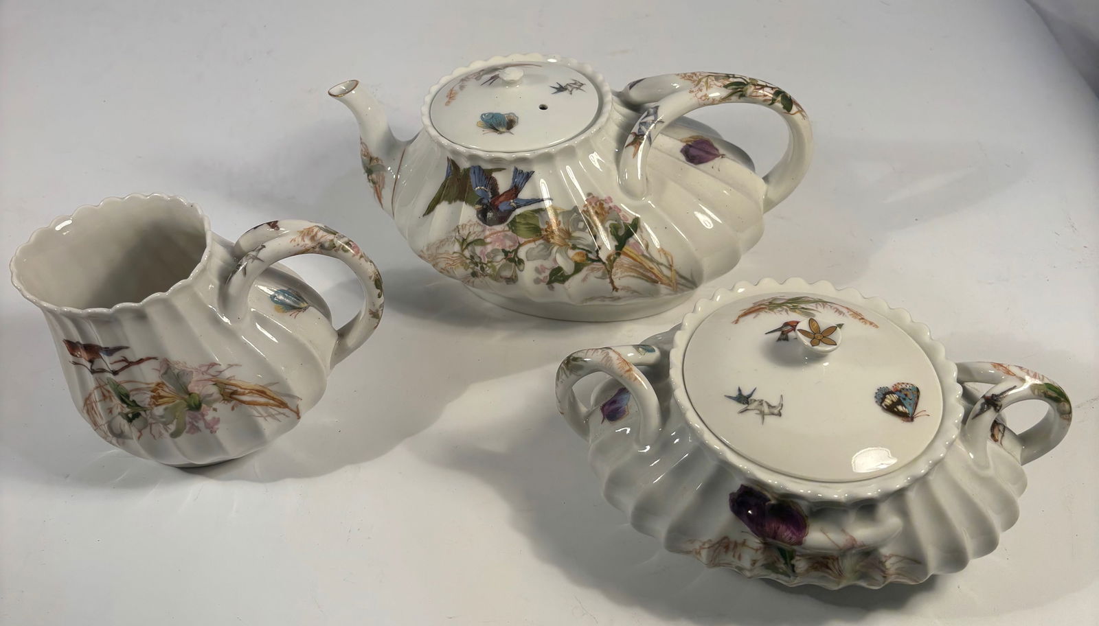 Haviland & Co. Limoges Hand-Painted Porcelain Tea Set with Birds and Flowers, c.1890 (3 Pcs): Charming Haviland & Co. Limoges porcelain tea set, circa 1890, comprising three (3) pieces: teapot with lid, covered sugar, and creamer. Each piece with paneled, scalloped form and finely hand-painted